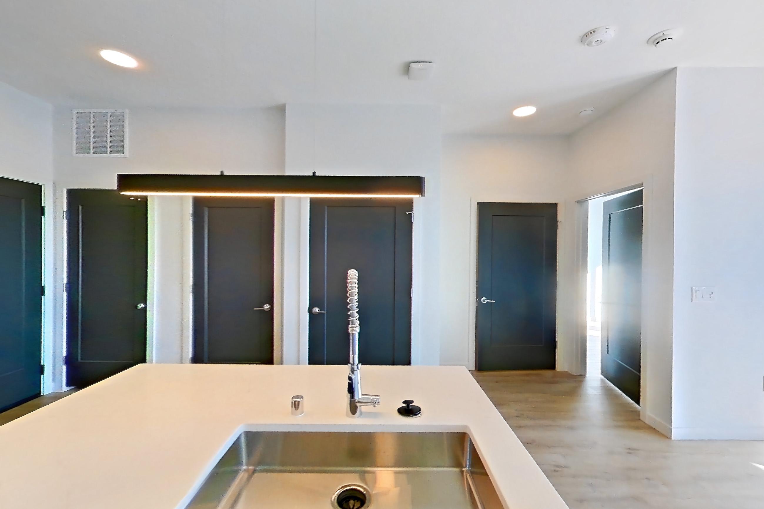 Kitchen with dishwasher, electric range, kitchen island, light countertops, light stone countertops, light wood-finish flooring, oven/range, refrigerator, stainless steel appliances, and water & ice dispenser, Apartment 411 at Gemma