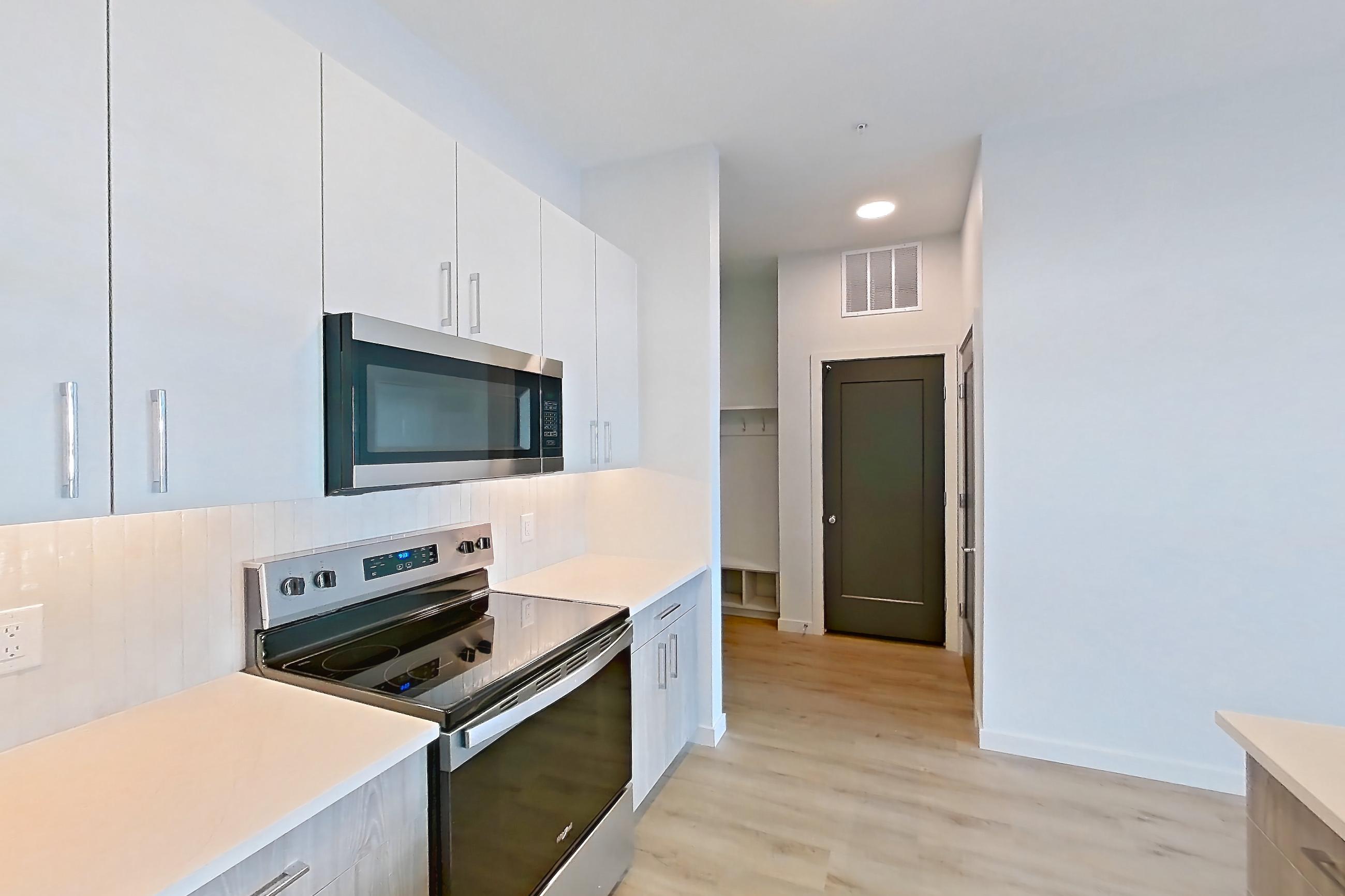 Kitchen with dishwasher, electric range, light countertops, light stone countertops, light wood-finish flooring, microwave, oven/range, refrigerator, stainless steel appliances, and water & ice dispenser, Apartment 428 at Gemma