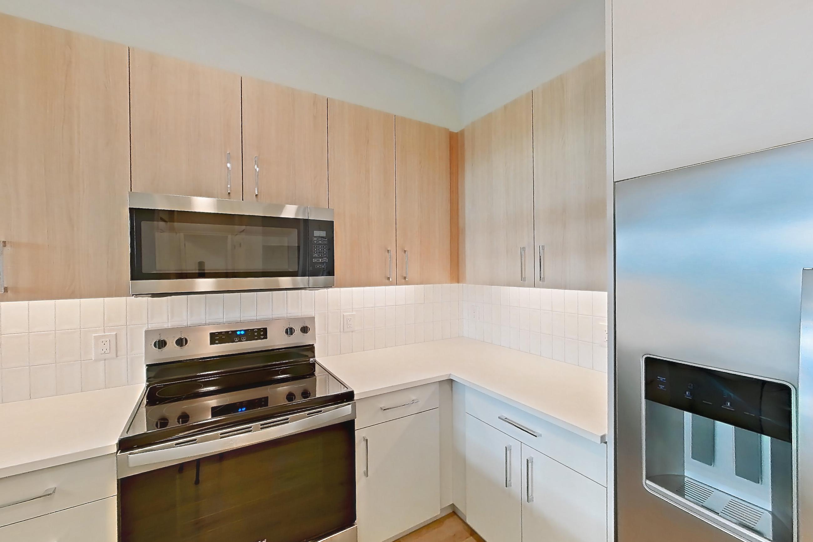 Kitchen with dishwasher, electric range, light countertops, light wood-finish flooring, microwave, oven/range, refrigerator, stainless steel appliances, and water & ice dispenser, Apartment 334 at Gemma