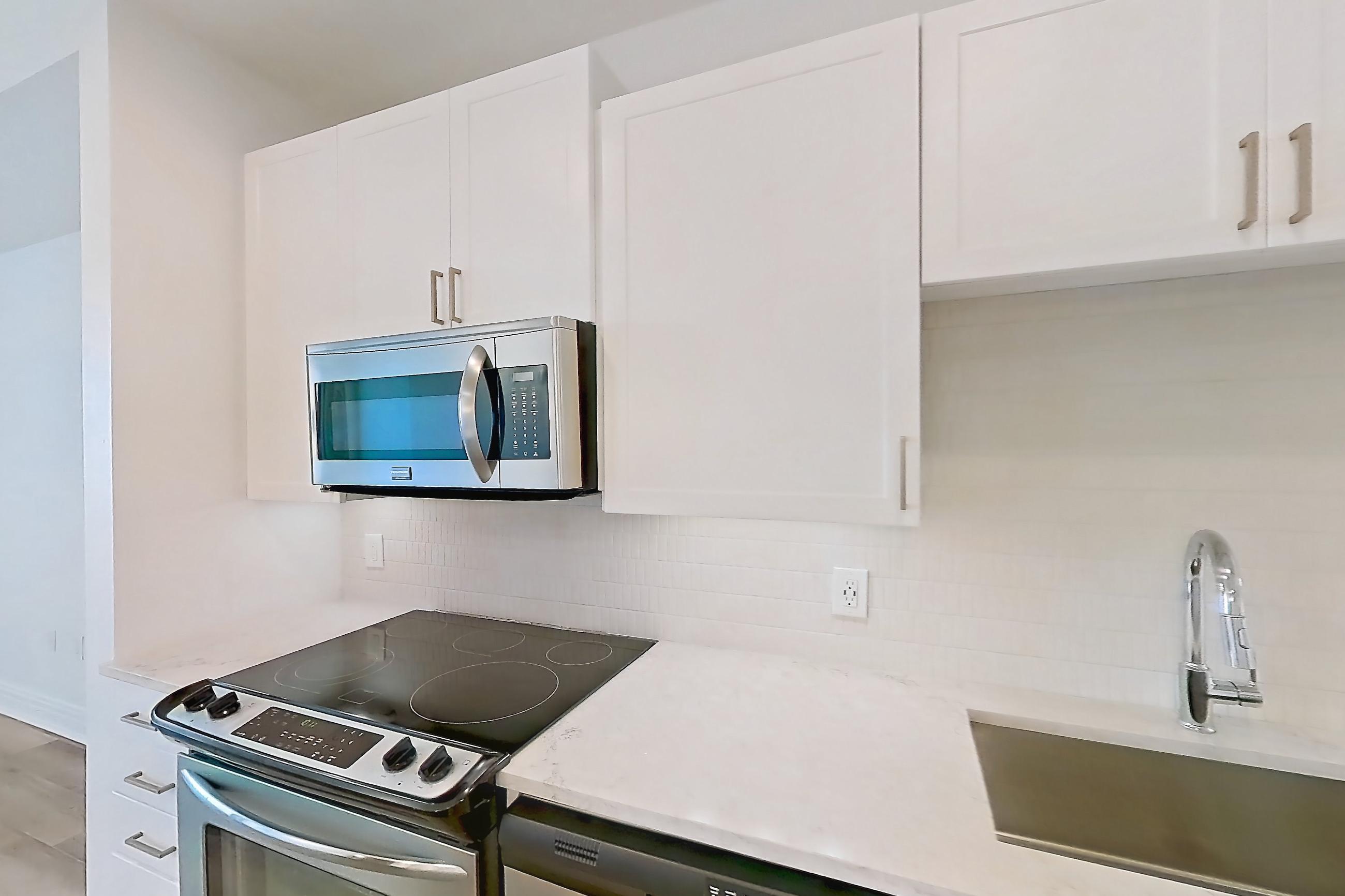 Kitchen with dishwasher, electric range, light countertops, light stone countertops, light wood-finish flooring, oven/range, refrigerator, stainless steel appliances, and water & ice dispenser, Apartment 1410 at 1400HiLine