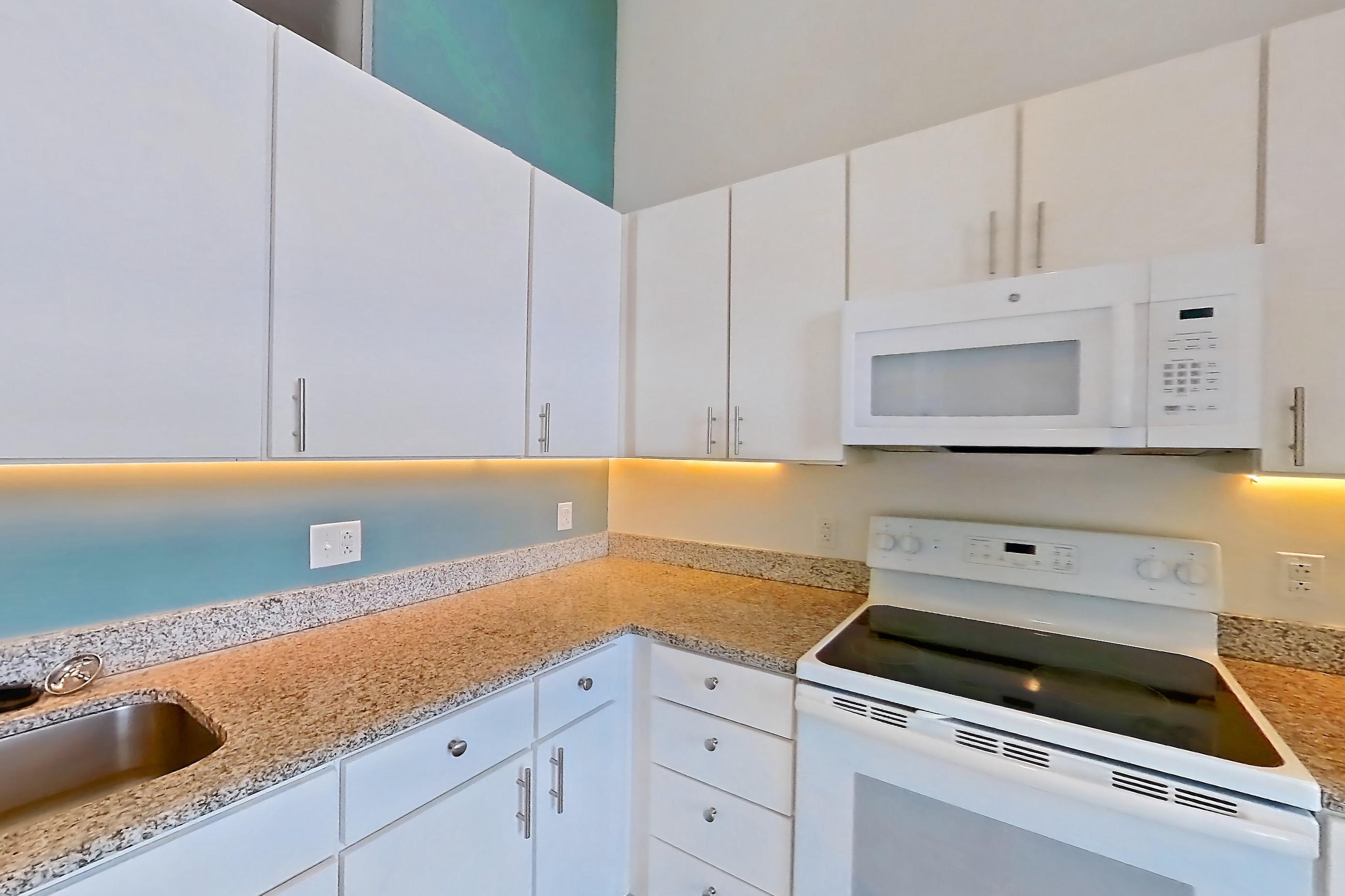 Kitchen with dishwasher, electric range, light concrete flooring, light countertops, light stone countertops, microwave, oven/range, refrigerator, and white appliances, Apartment 1013 at Parcels at Concourse