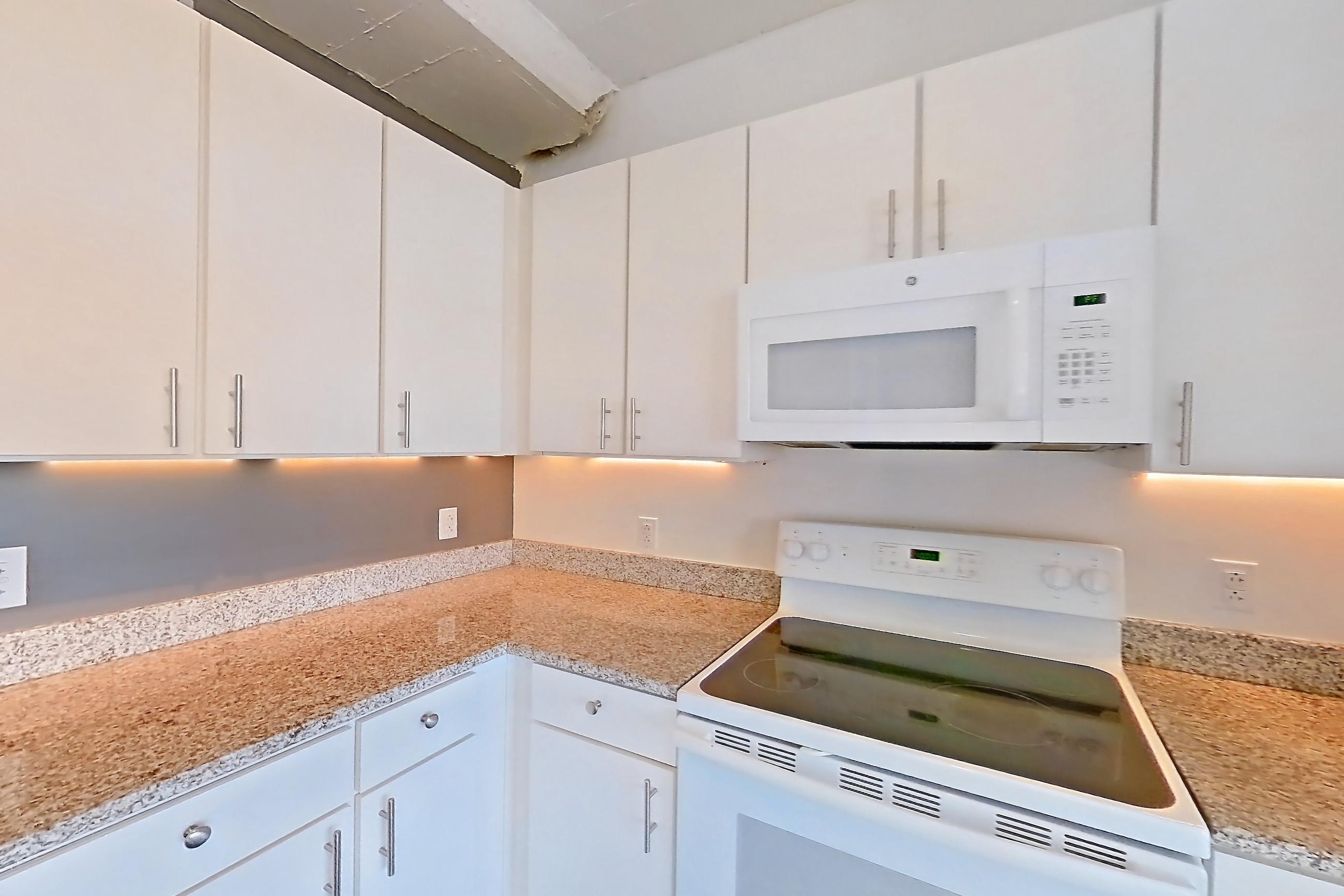 Kitchen with dark wood-finish flooring, dishwasher, electric range, light countertops, light stone countertops, microwave, oven/range, refrigerator, and white appliances, Apartment 729 at Parcels at Concourse