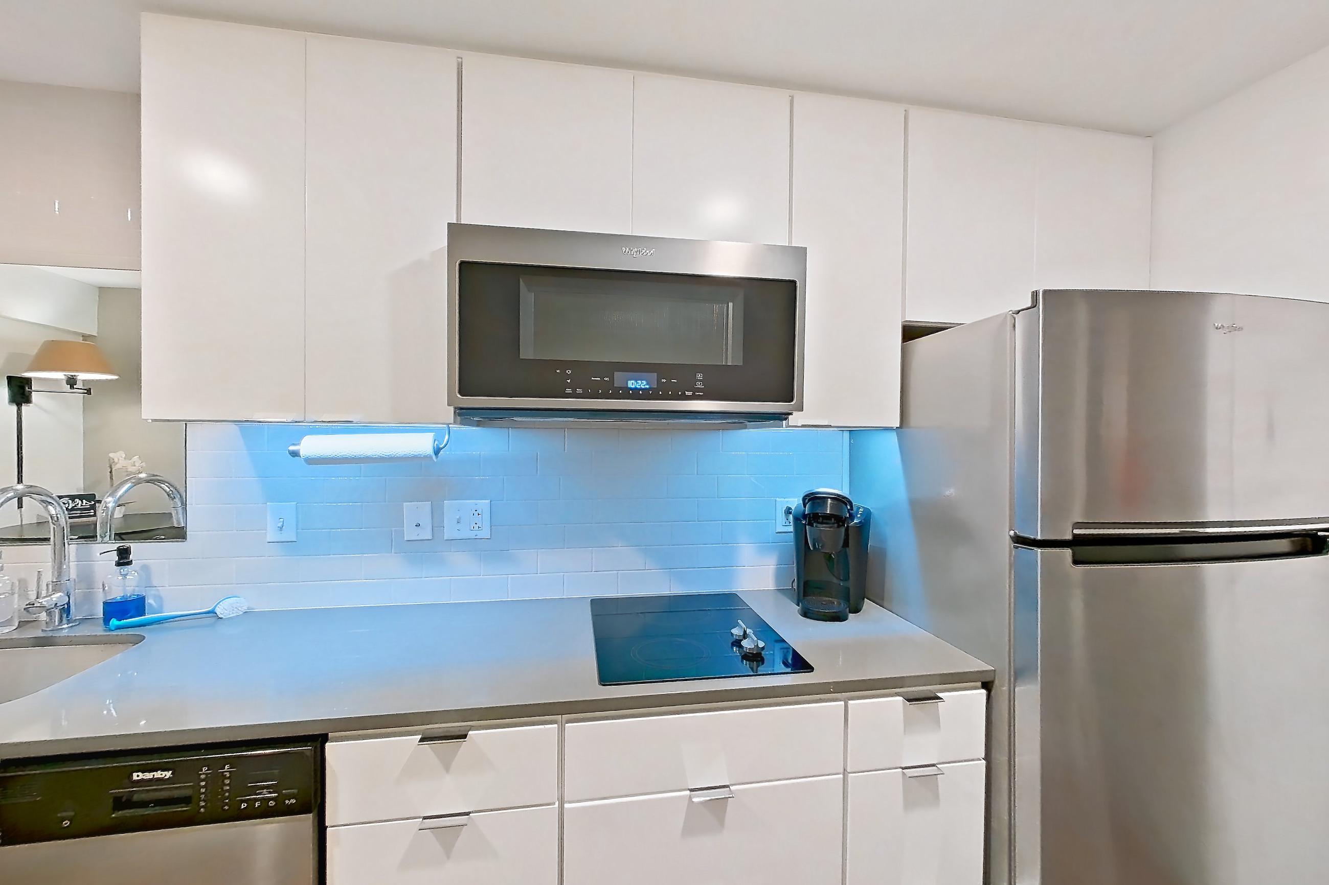 Kitchen with black appliances, cooktop, dark wood-finish flooring, dishwasher, electric cooktop, light countertops, refrigerator, and stainless steel appliances, Apartment 1-313 at Netherland and Monarch