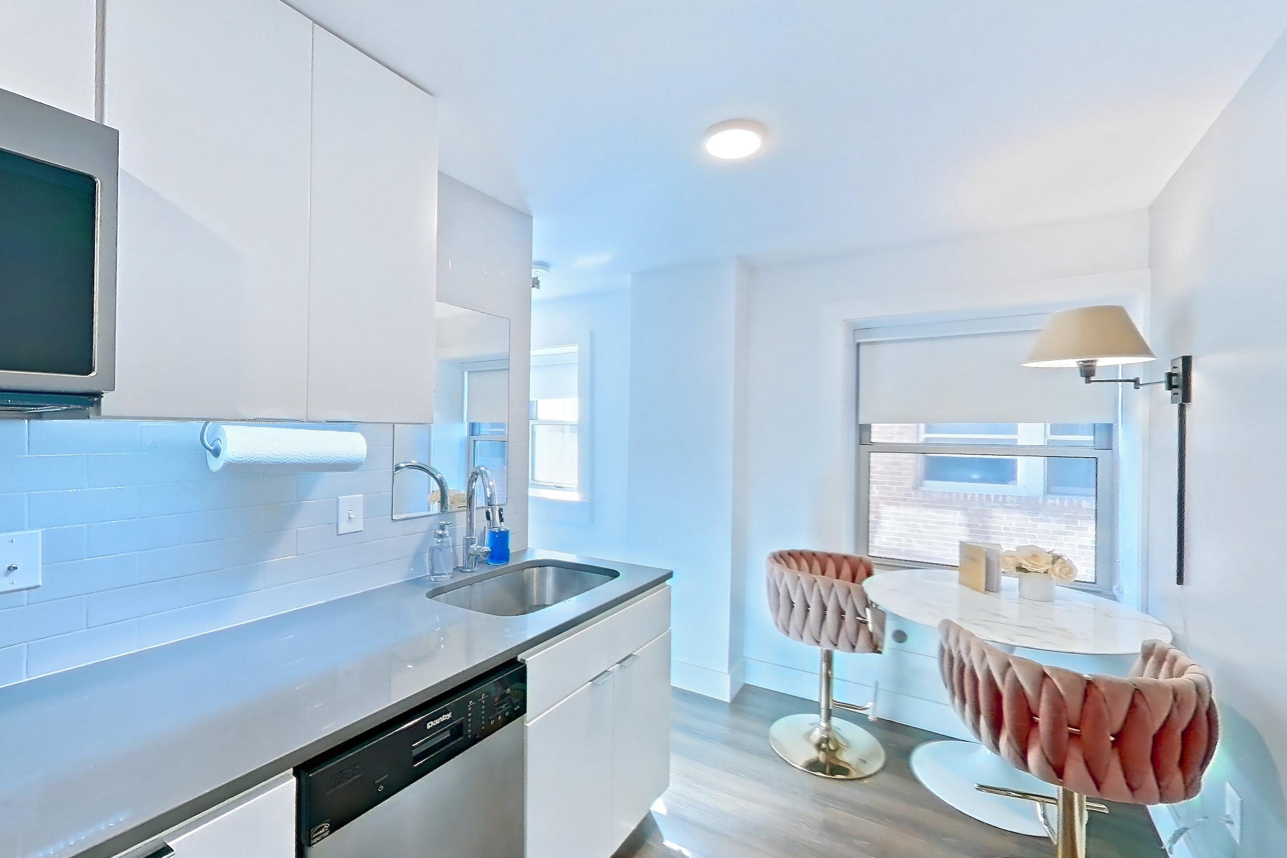 Kitchen with black appliances, cooktop, dark stone countertops, dark wood-finish flooring, dishwasher, electric cooktop, light countertops, refrigerator, and stainless steel appliances, Apartment 1-409 at Netherland and Monarch