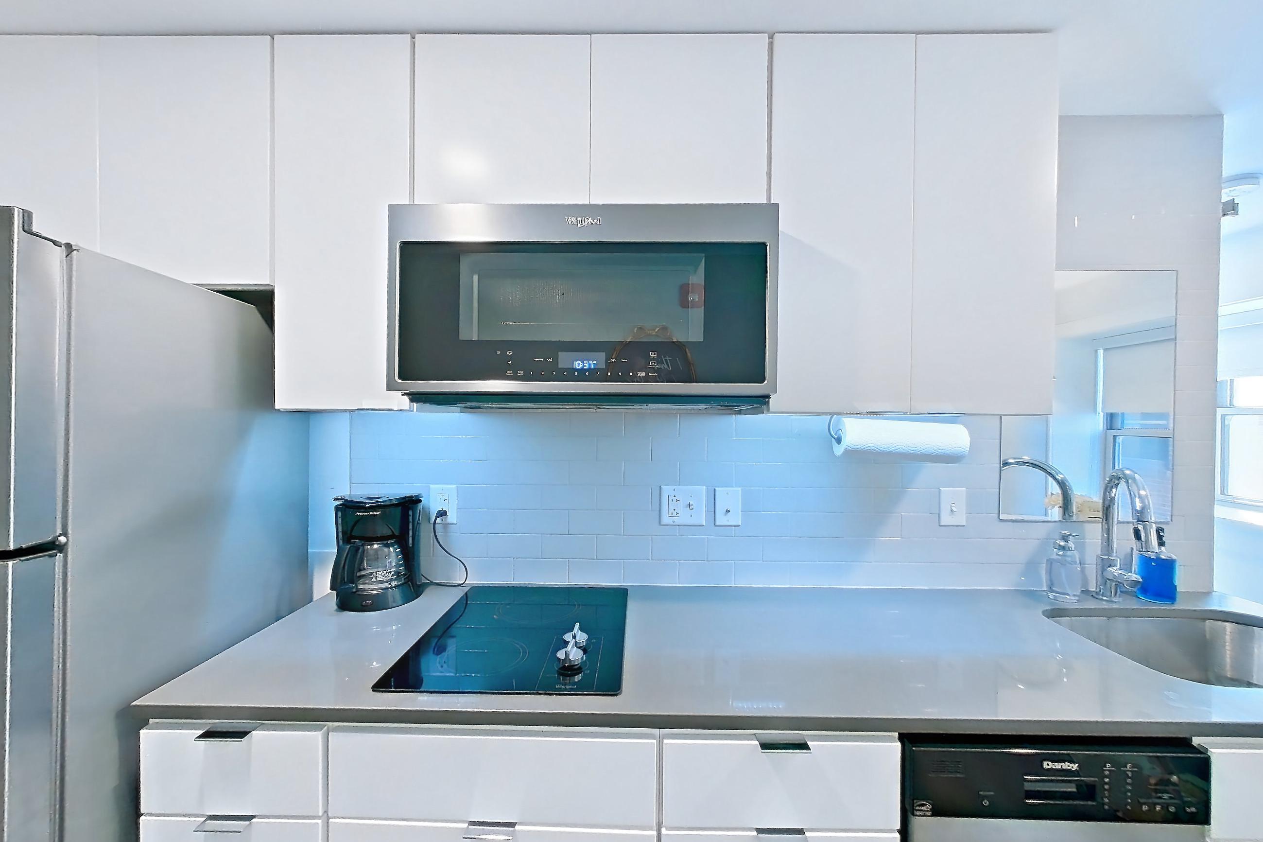 Kitchen with black appliances, cooktop, dark stone countertops, dark wood-finish flooring, dishwasher, electric cooktop, light countertops, refrigerator, and stainless steel appliances, Apartment 1-409 at Netherland and Monarch