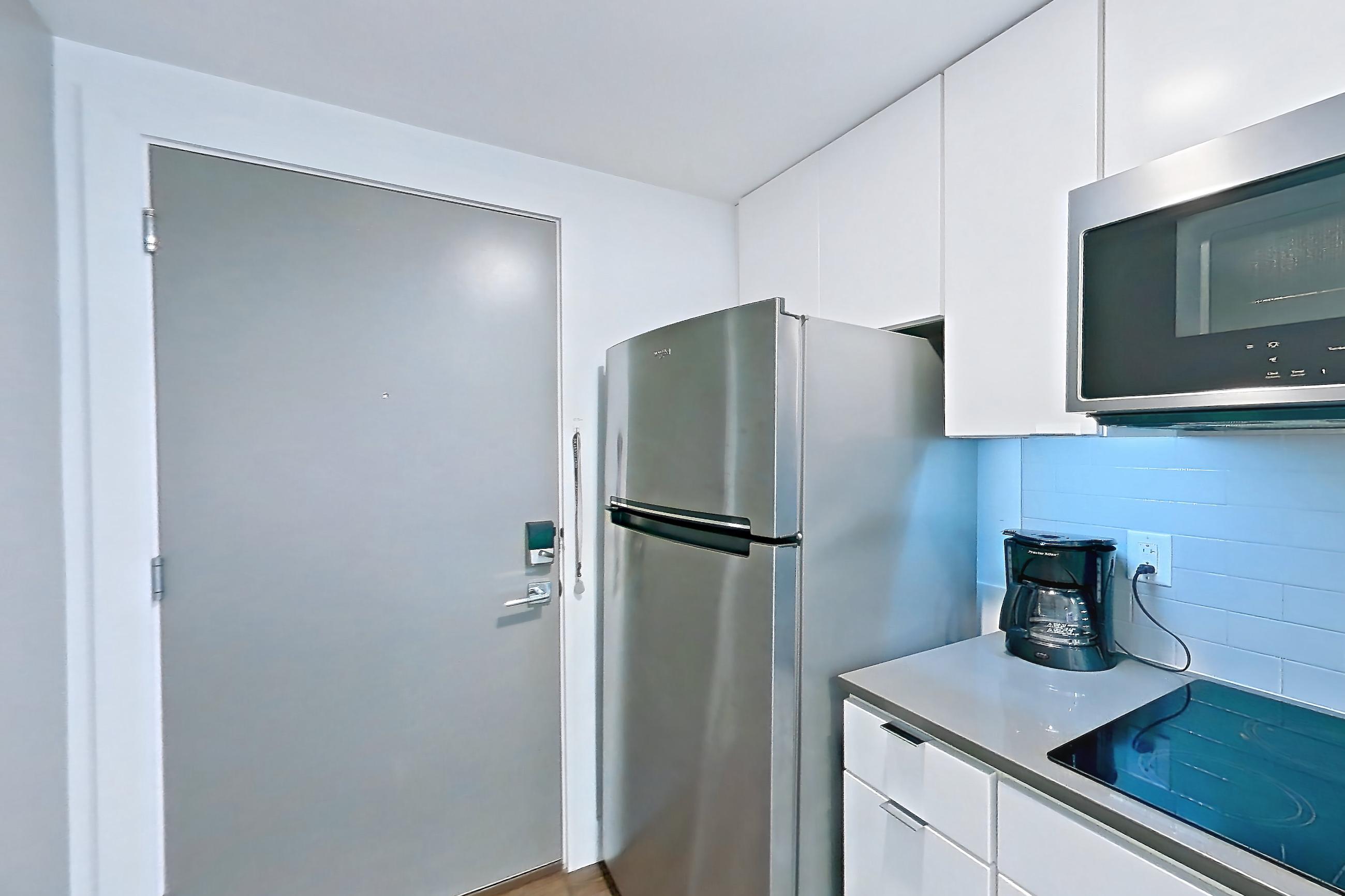 Kitchen with black appliances, cooktop, dark stone countertops, dark wood-finish flooring, dishwasher, electric cooktop, light countertops, refrigerator, and stainless steel appliances, Apartment 1-409 at Netherland and Monarch