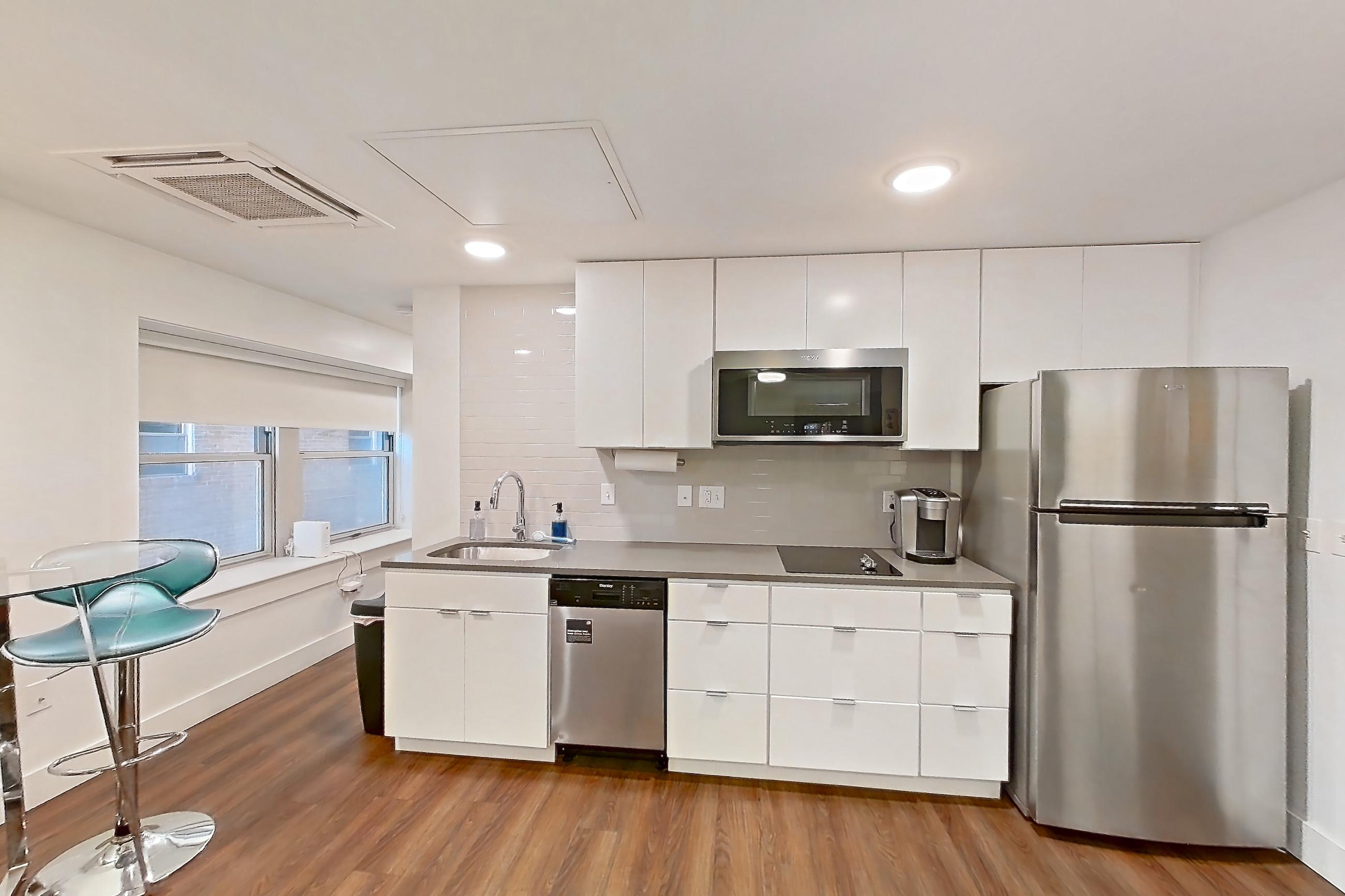 Living space with black appliances, cooktop, dark wood-finish flooring, dishwasher, electric cooktop, light countertops, microwave, refrigerator, stainless steel appliances, and white appliances, Apartment 1-411 at Netherland and Monarch