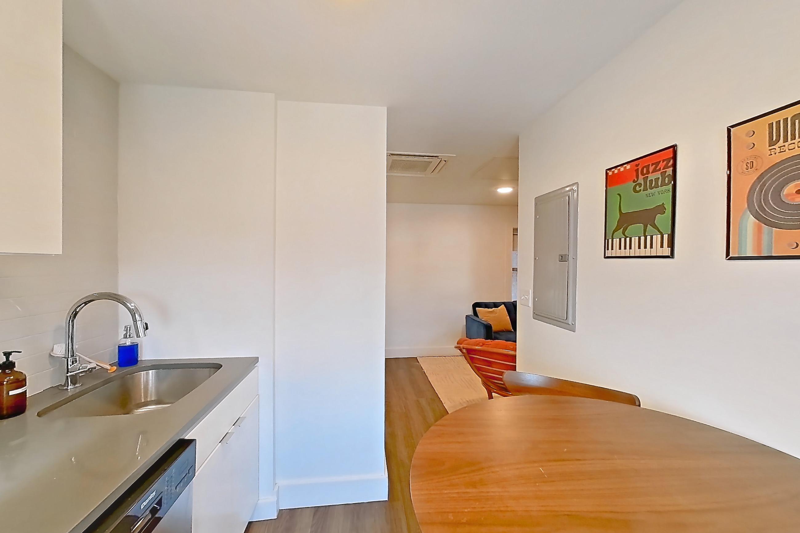 Kitchen with black appliances, cooktop, dishwasher, electric cooktop, light countertops, light wood-finish flooring, and stainless steel appliances, Apartment 1-415 at Netherland and Monarch