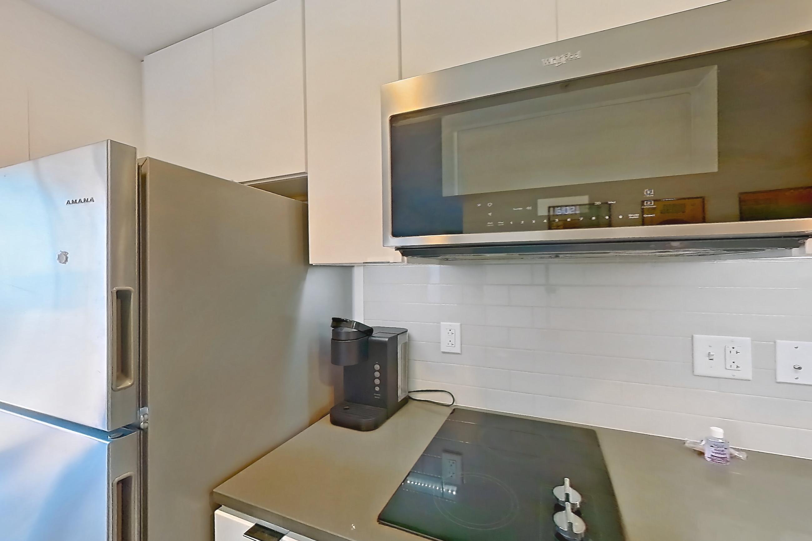 Kitchen with black appliances, cooktop, dishwasher, electric cooktop, light countertops, light wood-finish flooring, and stainless steel appliances, Apartment 1-415 at Netherland and Monarch