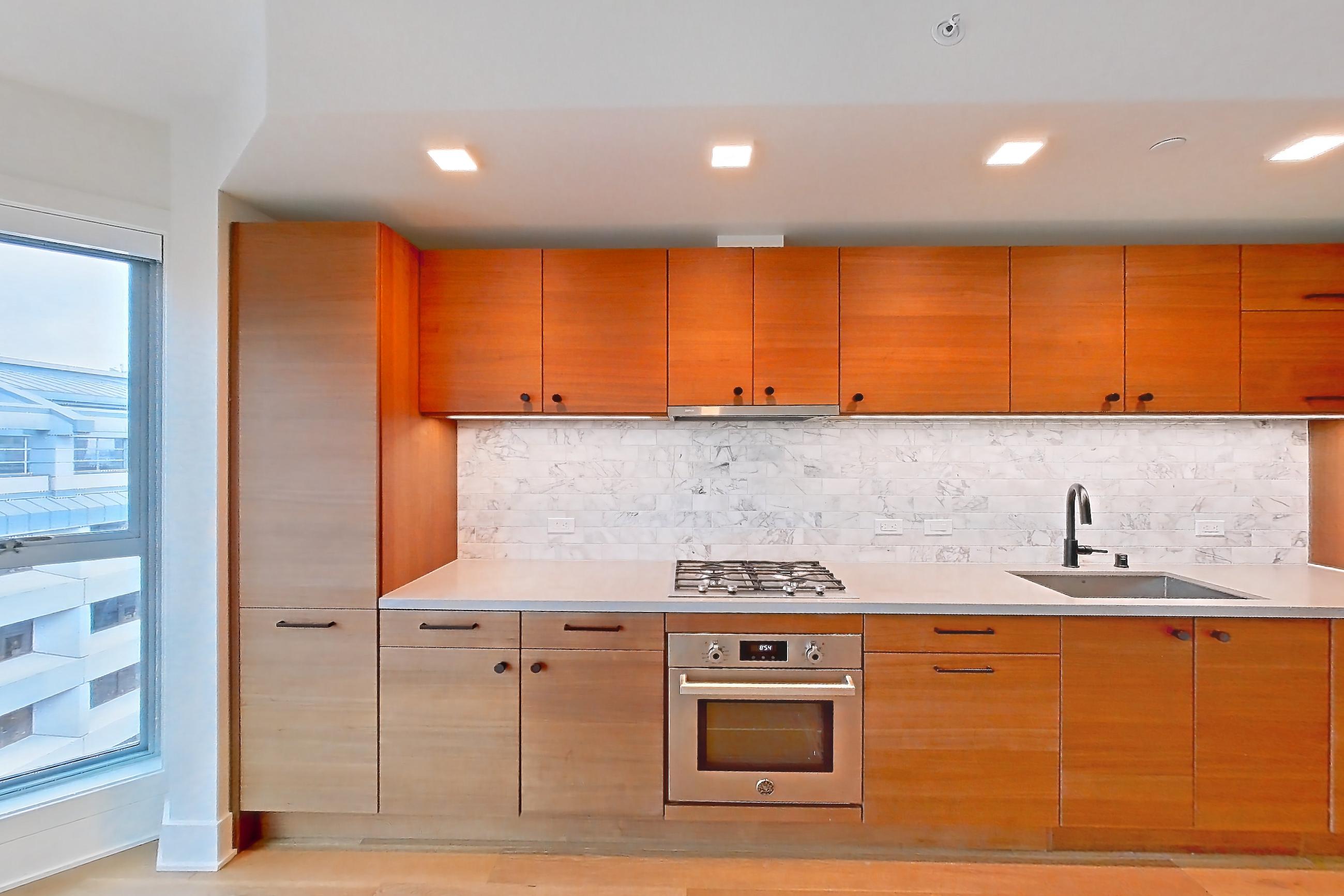 Kitchen with cooktop, gas cooktop, light countertops, light stone countertops, light wood-finish flooring, oven/range, range hood, stainless steel appliances, and sunroom, Apartment 605 at Konrad on the Park