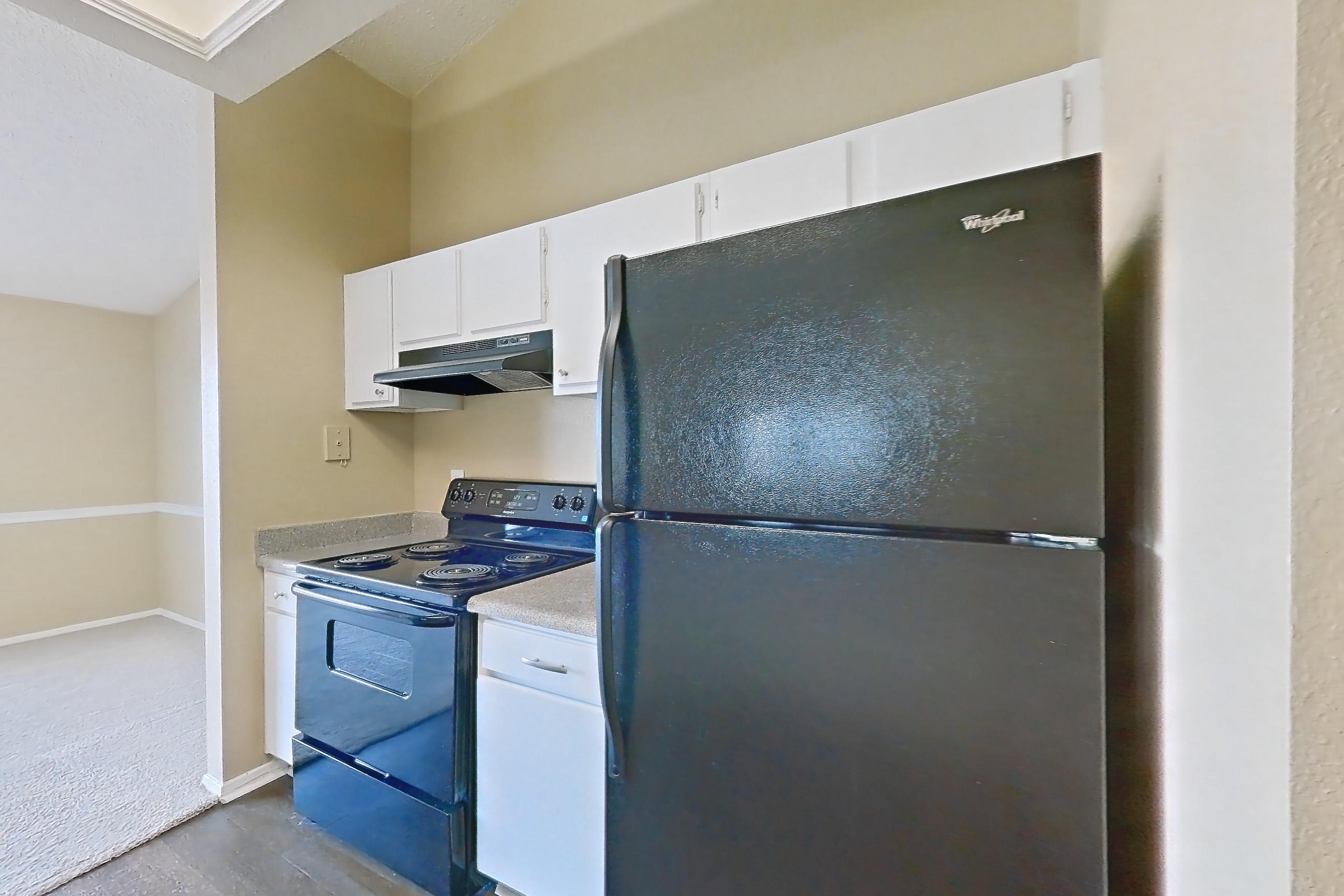 Kitchen with black appliances, dark wood-finish flooring, dishwasher, electric range, in-unit laundry, light countertops, oven/range, range hood, refrigerator, and white appliances, Apartment 921 at Museo and Channings Mark