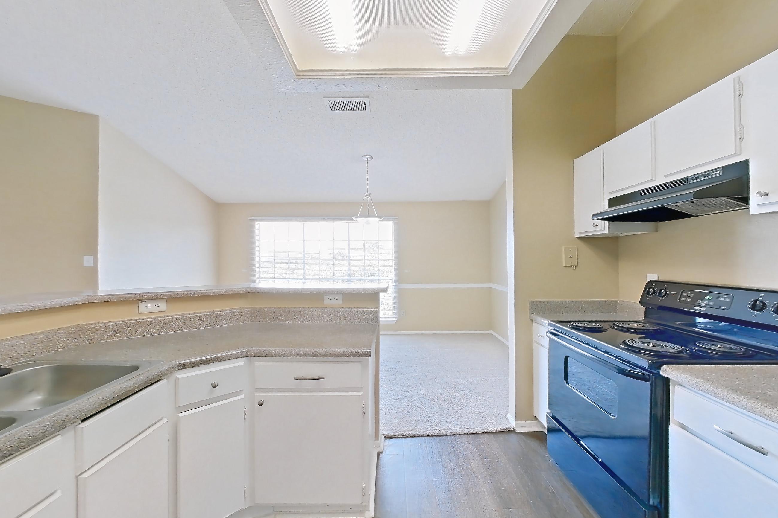 Kitchen with black appliances, dark wood-finish flooring, dishwasher, electric range, in-unit laundry, light countertops, oven/range, range hood, refrigerator, and white appliances, Apartment 921 at Museo and Channings Mark