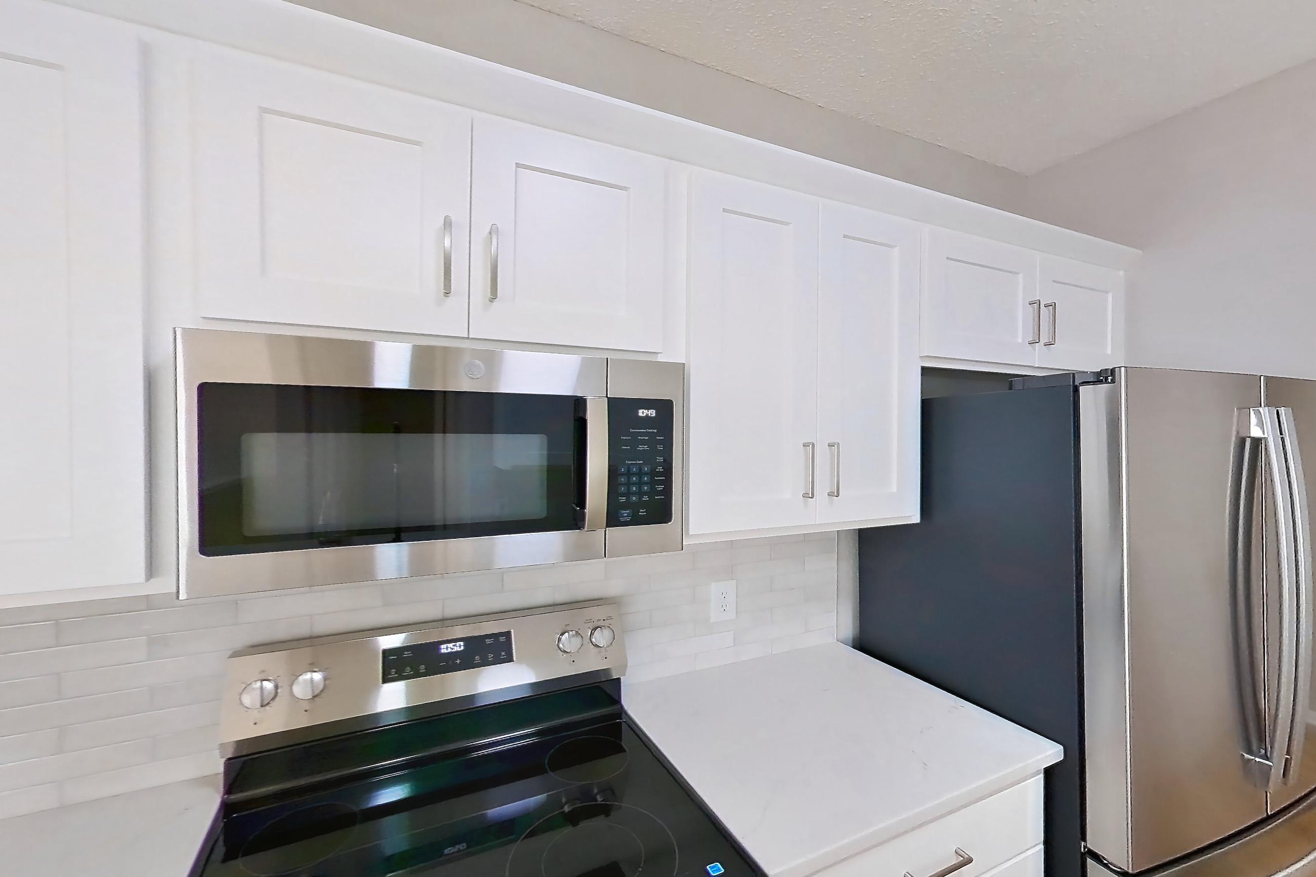 Kitchen with dishwasher, electric range, light countertops, light stone countertops, light wood-finish flooring, microwave, oven/range, refrigerator, and stainless steel appliances, Apartment Walkout Townhome at Bradford Pointe