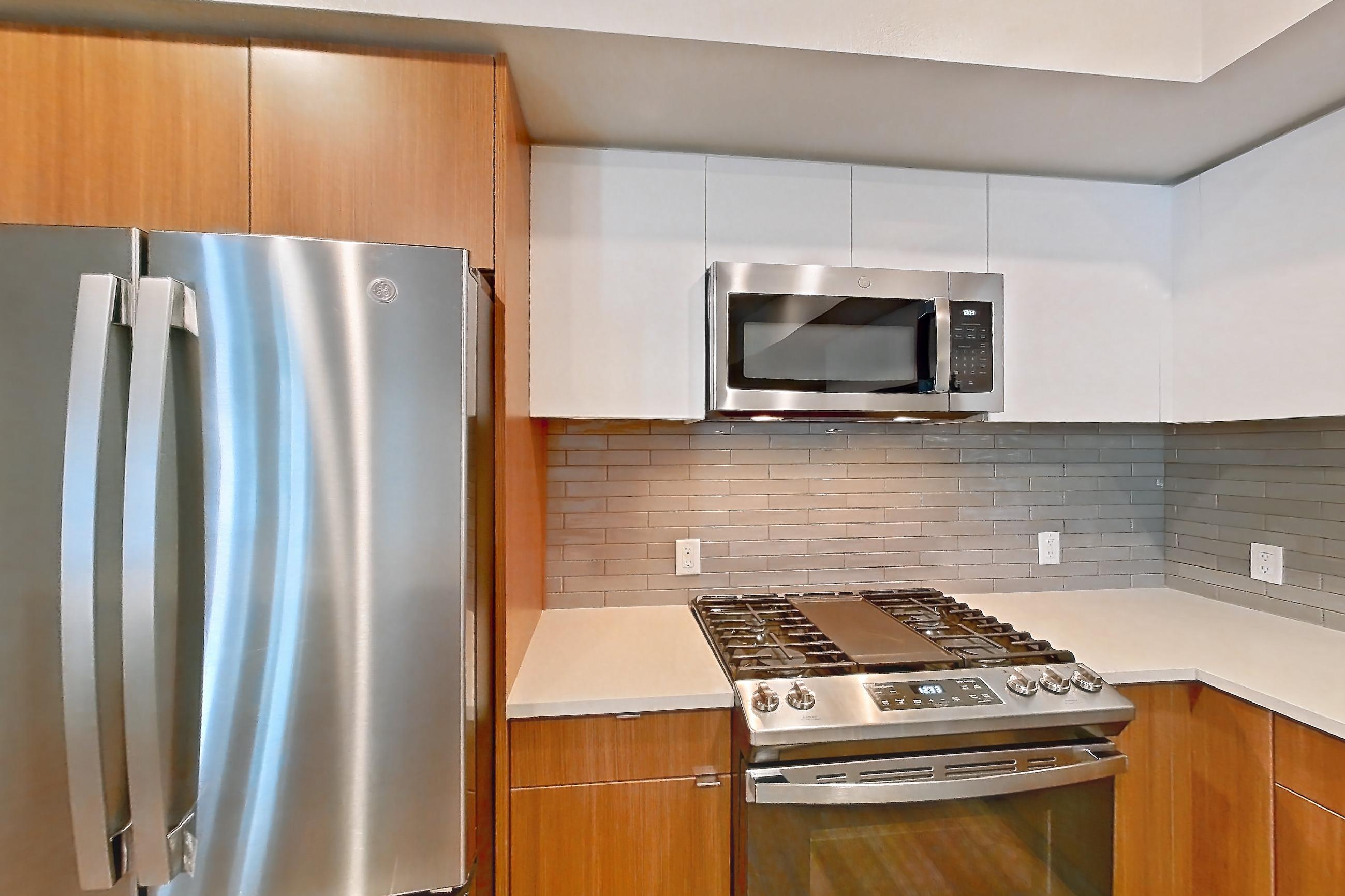Kitchen with dishwasher, gas range, light countertops, light stone countertops, light wood-finish flooring, microwave, oven/range, refrigerator, and stainless steel appliances, Apartment 503 at Assembly