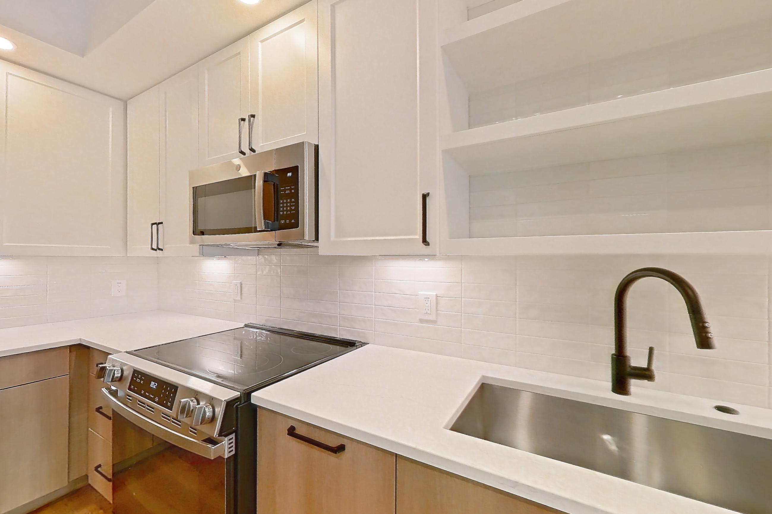 Kitchen with black appliances, dishwasher, electric range, light countertops, light stone countertops, light wood-finish flooring, oven/range, and stainless steel appliances, Apartment 311 at The Watson