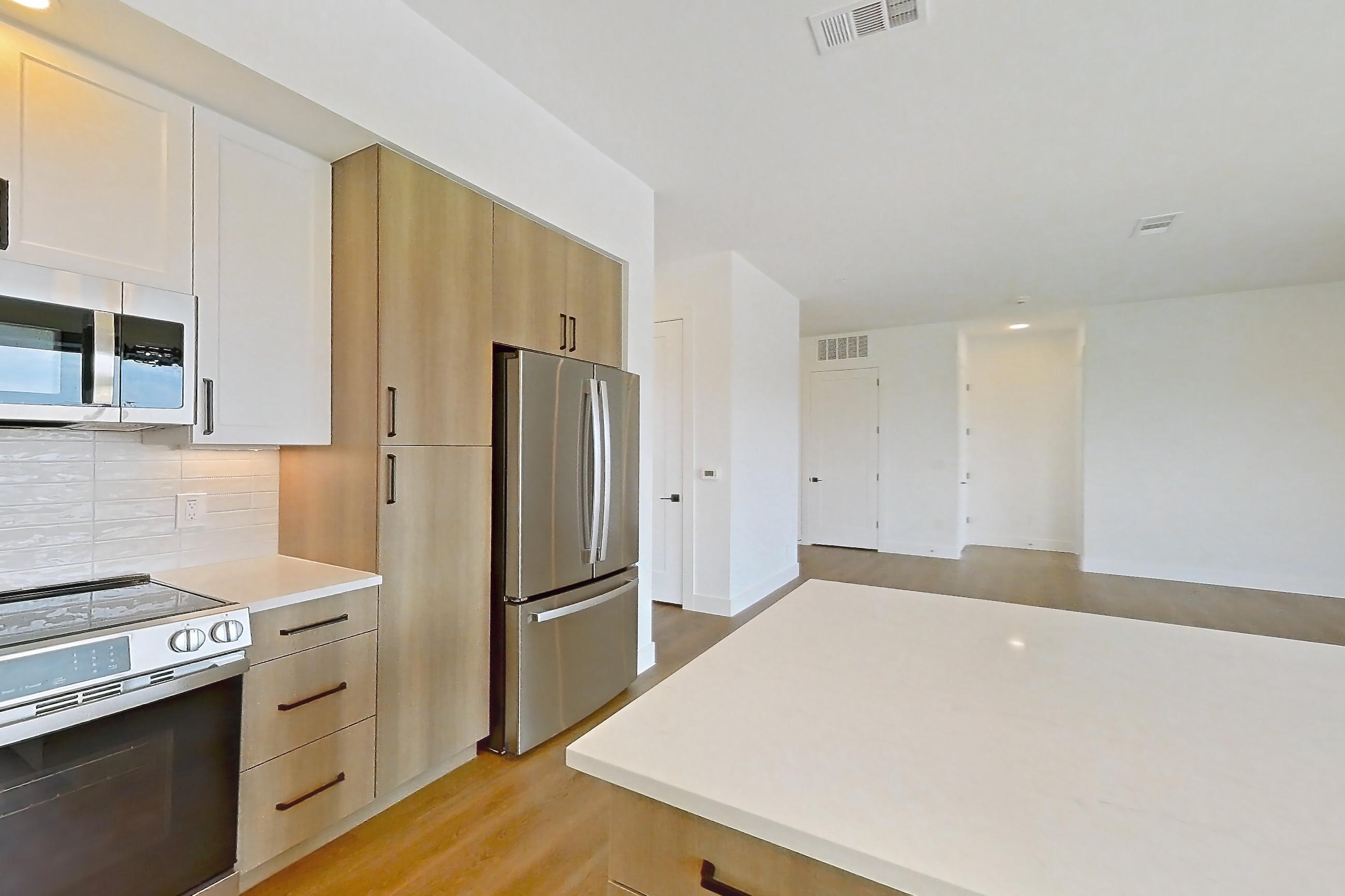 Kitchen with dishwasher, light stone countertops, light wood-finish flooring, refrigerator, and stainless steel appliances, Apartment 316 at The Watson