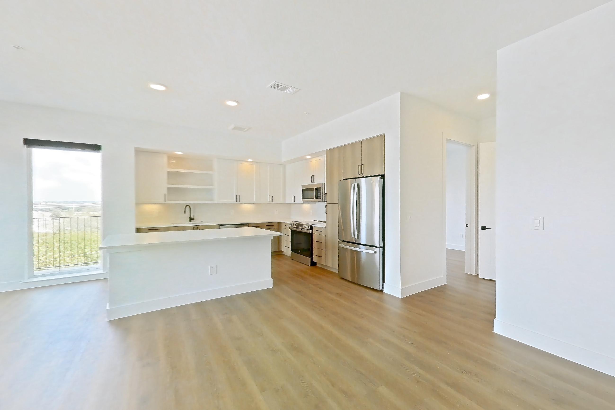 Living space with electric range, light countertops, light wood-finish flooring, oven/range, refrigerator, and stainless steel appliances, Apartment 316 at The Watson