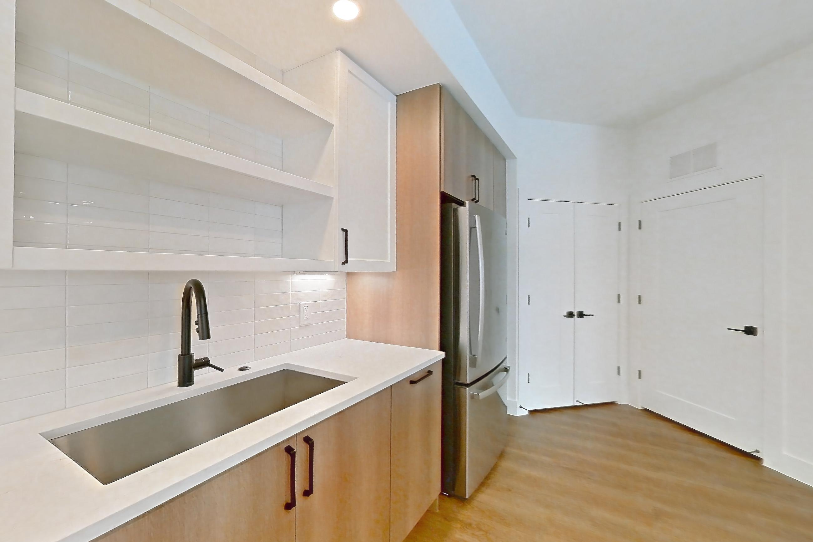 Kitchen with electric range, light countertops, light stone countertops, light wood-finish flooring, oven/range, refrigerator, and stainless steel appliances, Apartment 401 at The Watson