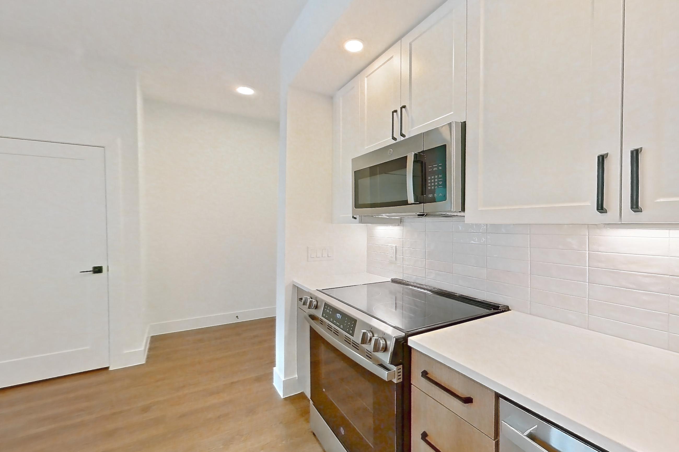 Kitchen with electric range, light countertops, light stone countertops, light wood-finish flooring, oven/range, refrigerator, and stainless steel appliances, Apartment 401 at The Watson