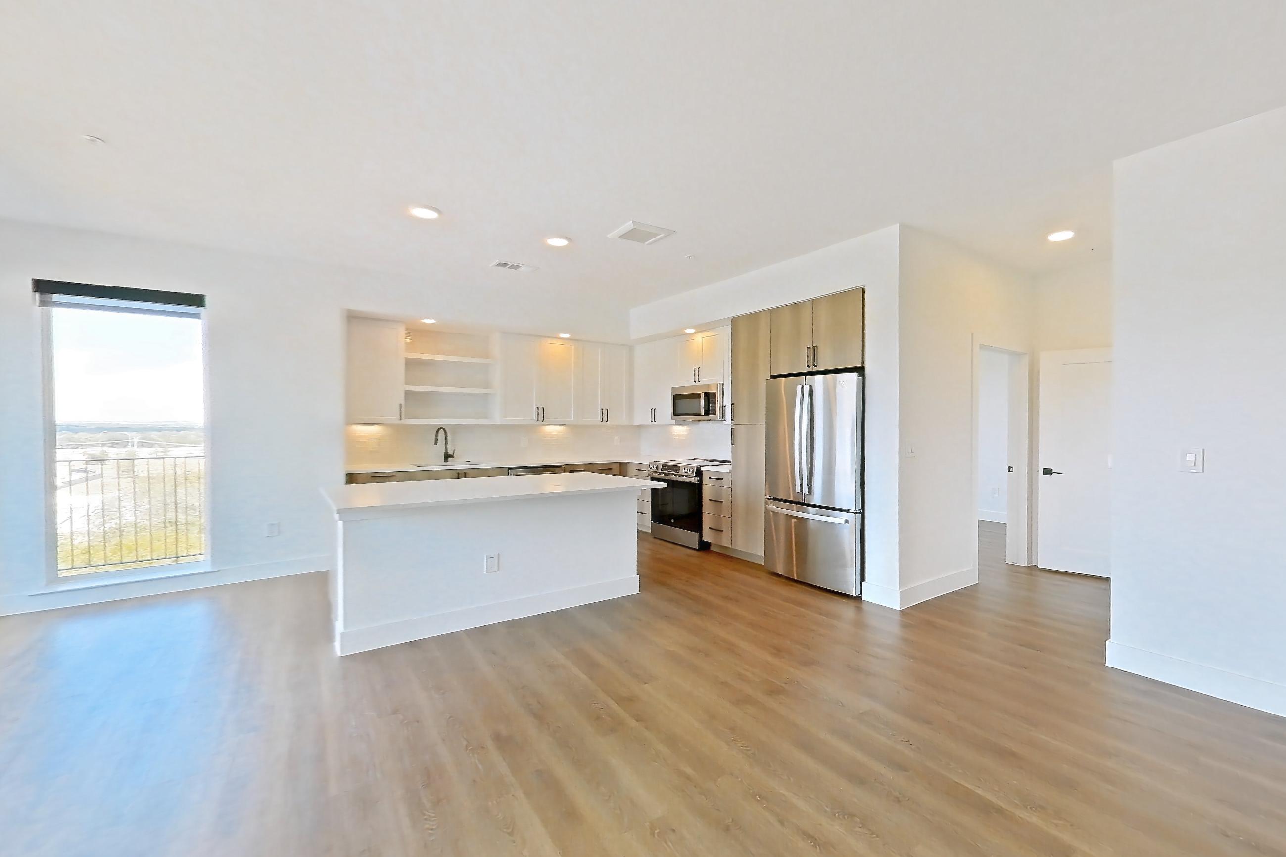 Living space with dark wood-finish flooring, electric range, light countertops, light wood-finish flooring, oven/range, refrigerator, and stainless steel appliances, Apartment 416 at The Watson