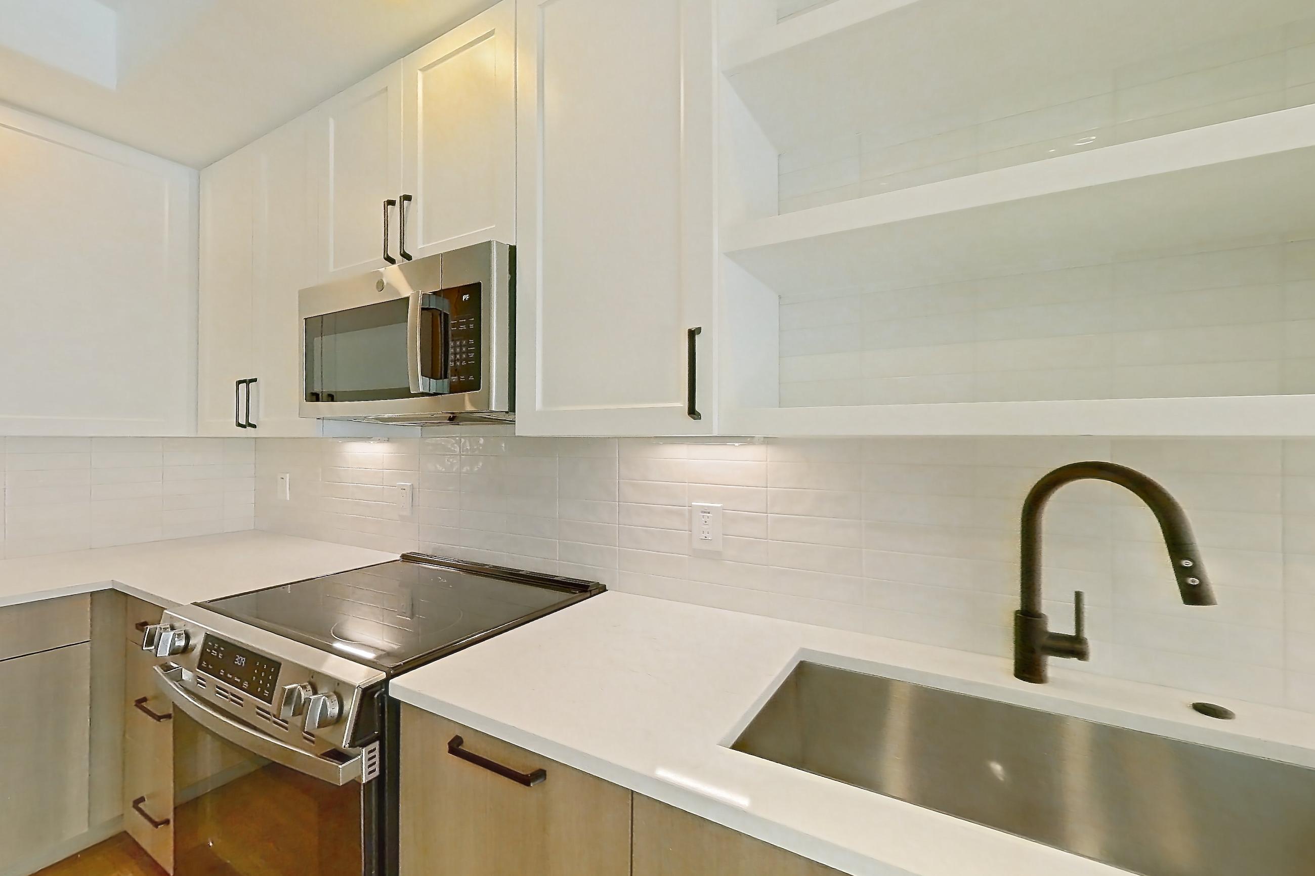 Kitchen with black appliances, dishwasher, electric range, light stone countertops, light wood-finish flooring, oven/range, and stainless steel appliances, Apartment 511 at The Watson