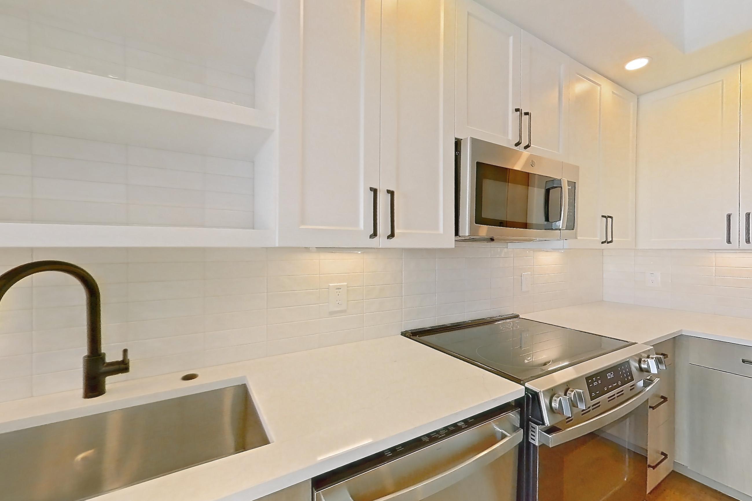 Kitchen with dishwasher, electric range, light stone countertops, light wood-finish flooring, and stainless steel appliances, Apartment 613 at The Watson