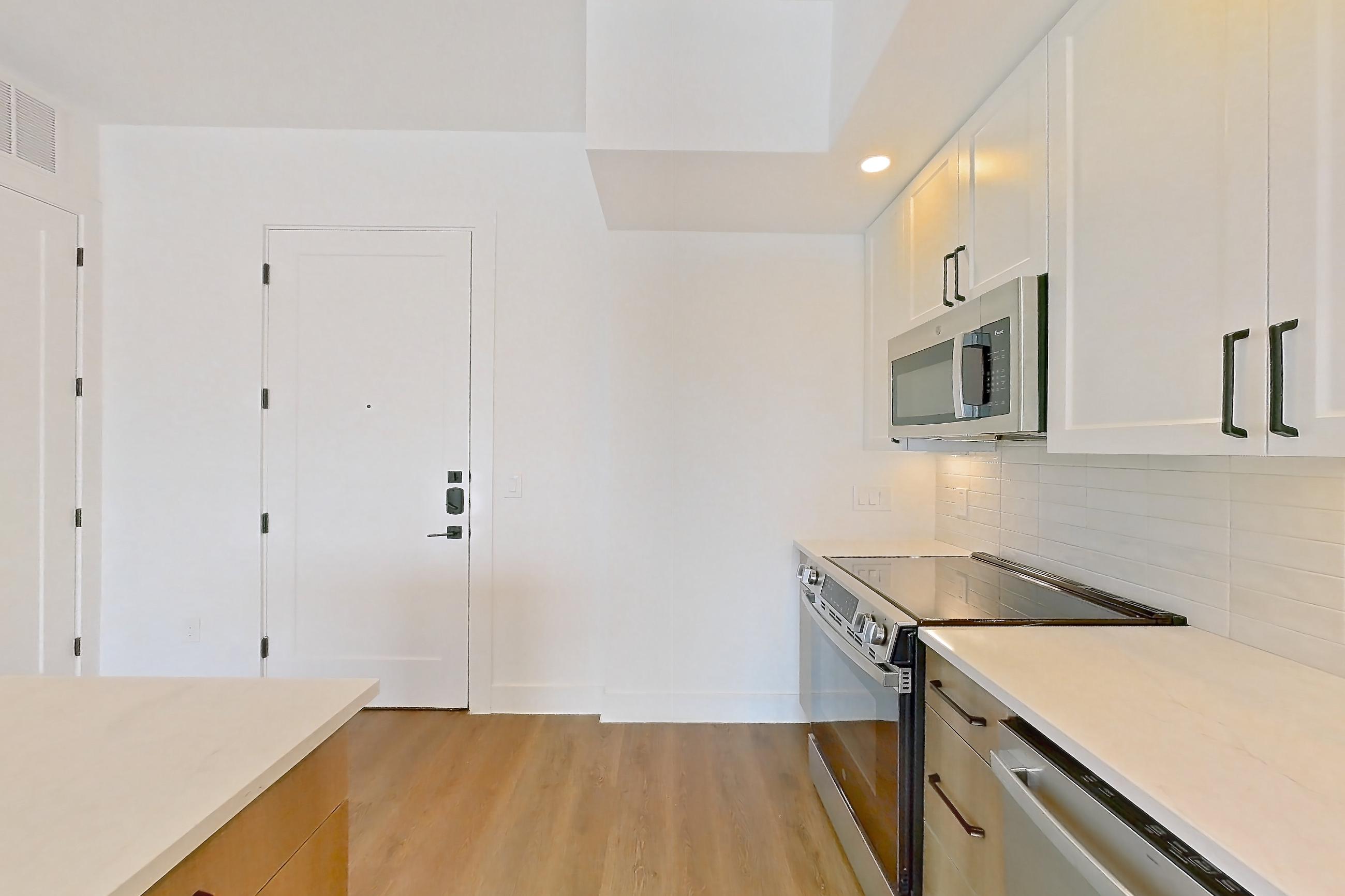 Kitchen with dishwasher, light countertops, light stone countertops, light wood-finish flooring, refrigerator, and stainless steel appliances, Apartment 615 at The Watson
