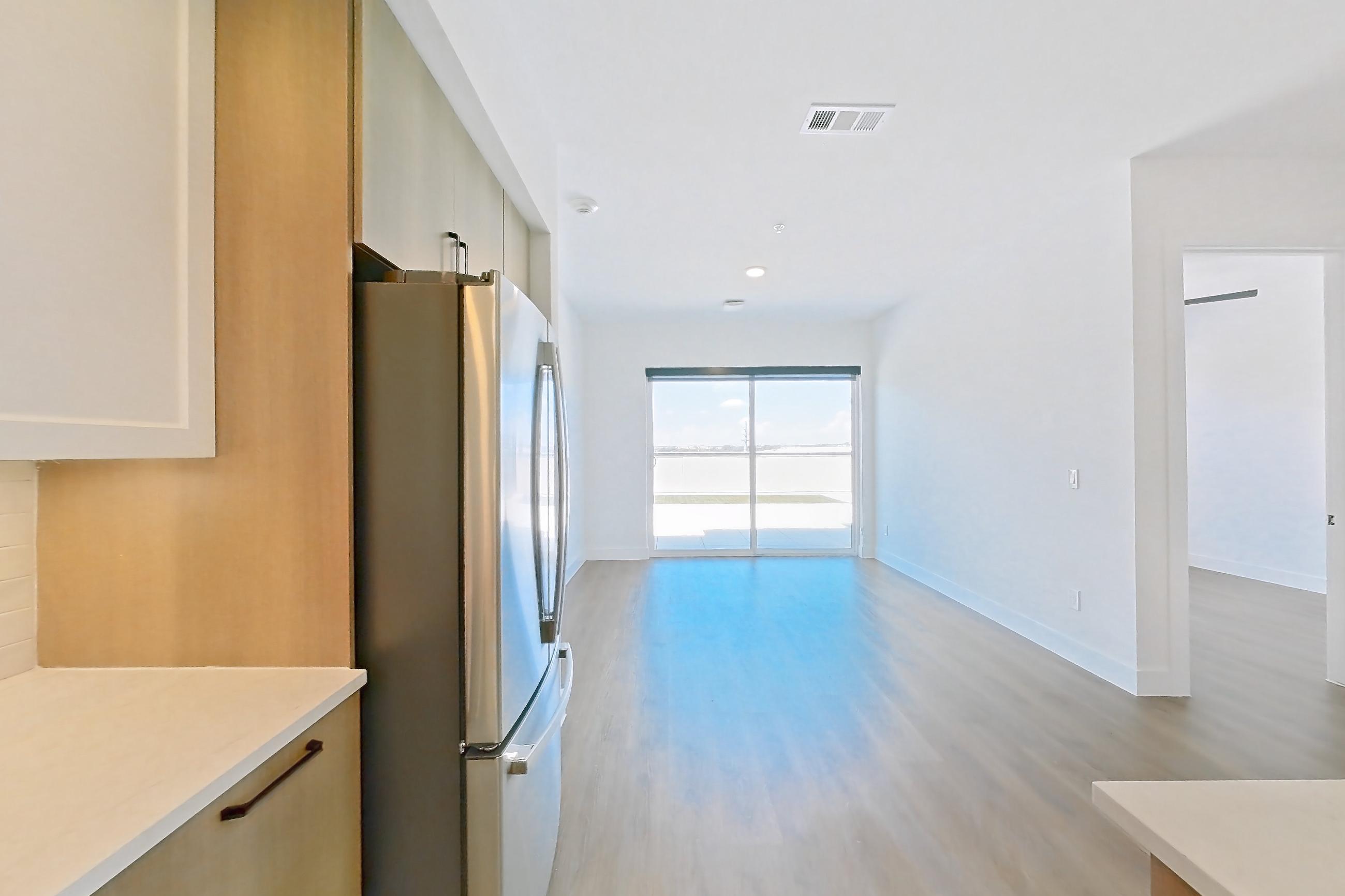 Kitchen with dishwasher, light countertops, light stone countertops, light wood-finish flooring, refrigerator, and stainless steel appliances, Apartment 615 at The Watson