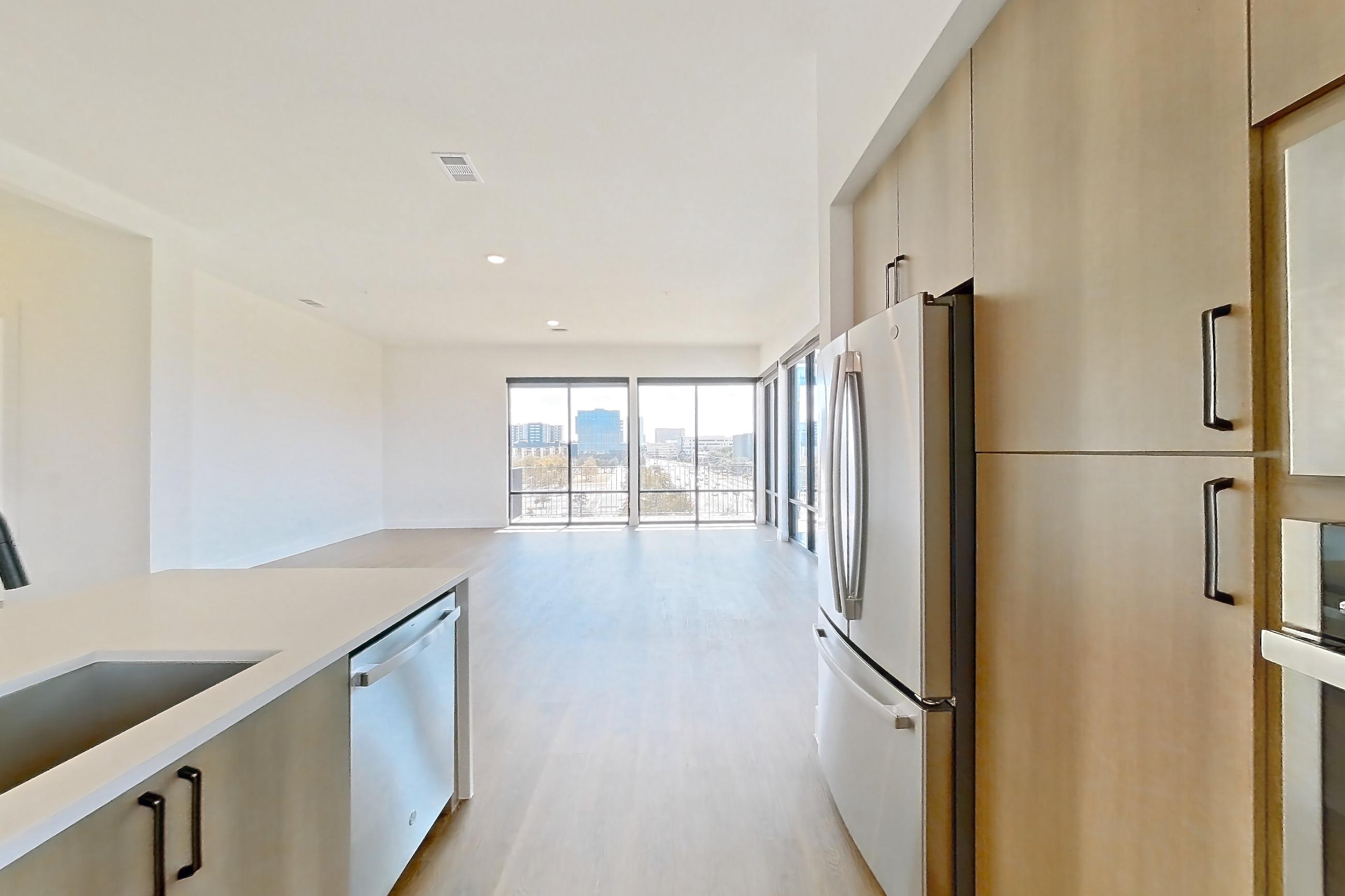 Kitchen with built-in microwave, dishwasher, light countertops, light stone countertops, light wood-finish flooring, microwave, oven/range, refrigerator, and stainless steel appliances, Apartment 703 at The Watson