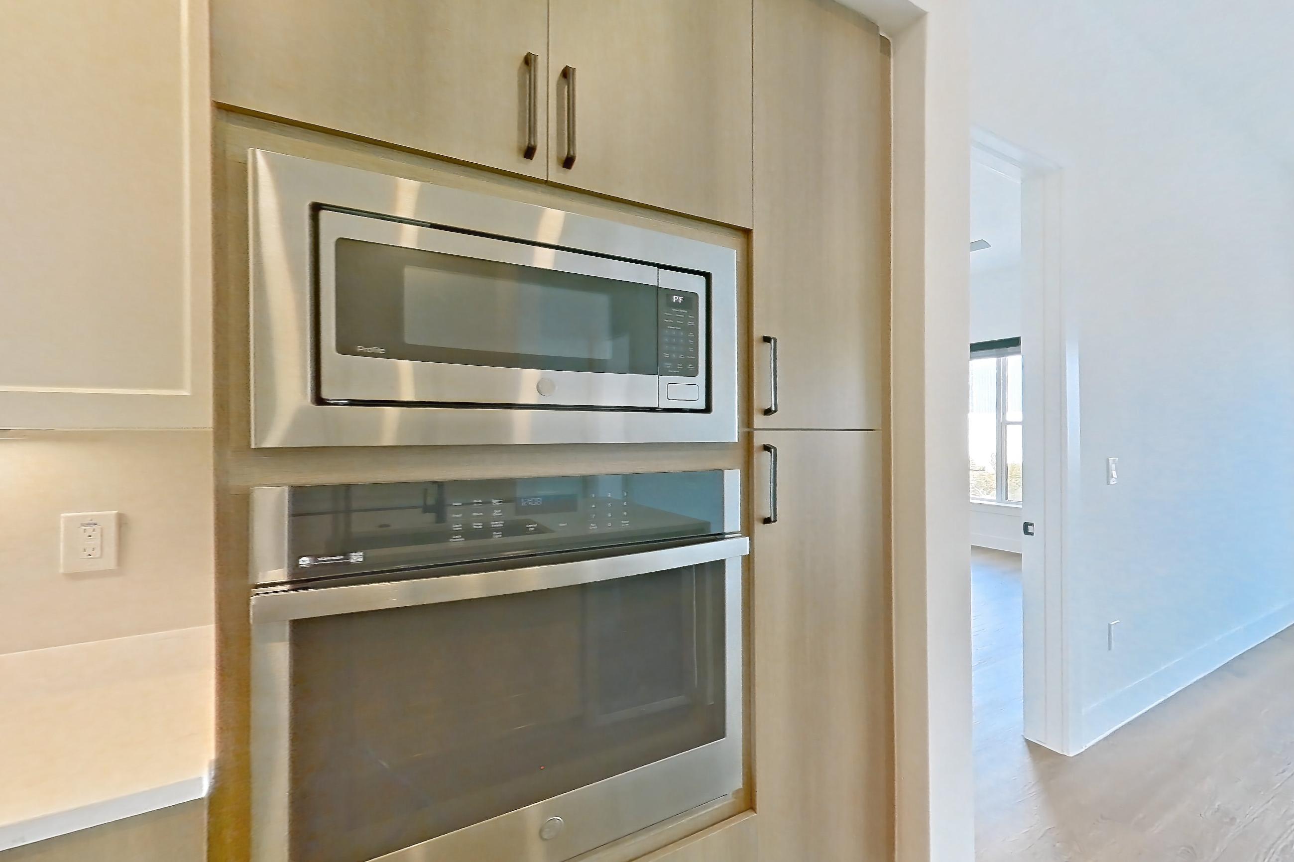 Kitchen with black appliances, built-in microwave, cooktop, electric cooktop, kitchen island, light countertops, light stone countertops, light wood-finish flooring, microwave, oven/range, and stainless steel appliances, Apartment 709 at The Watson