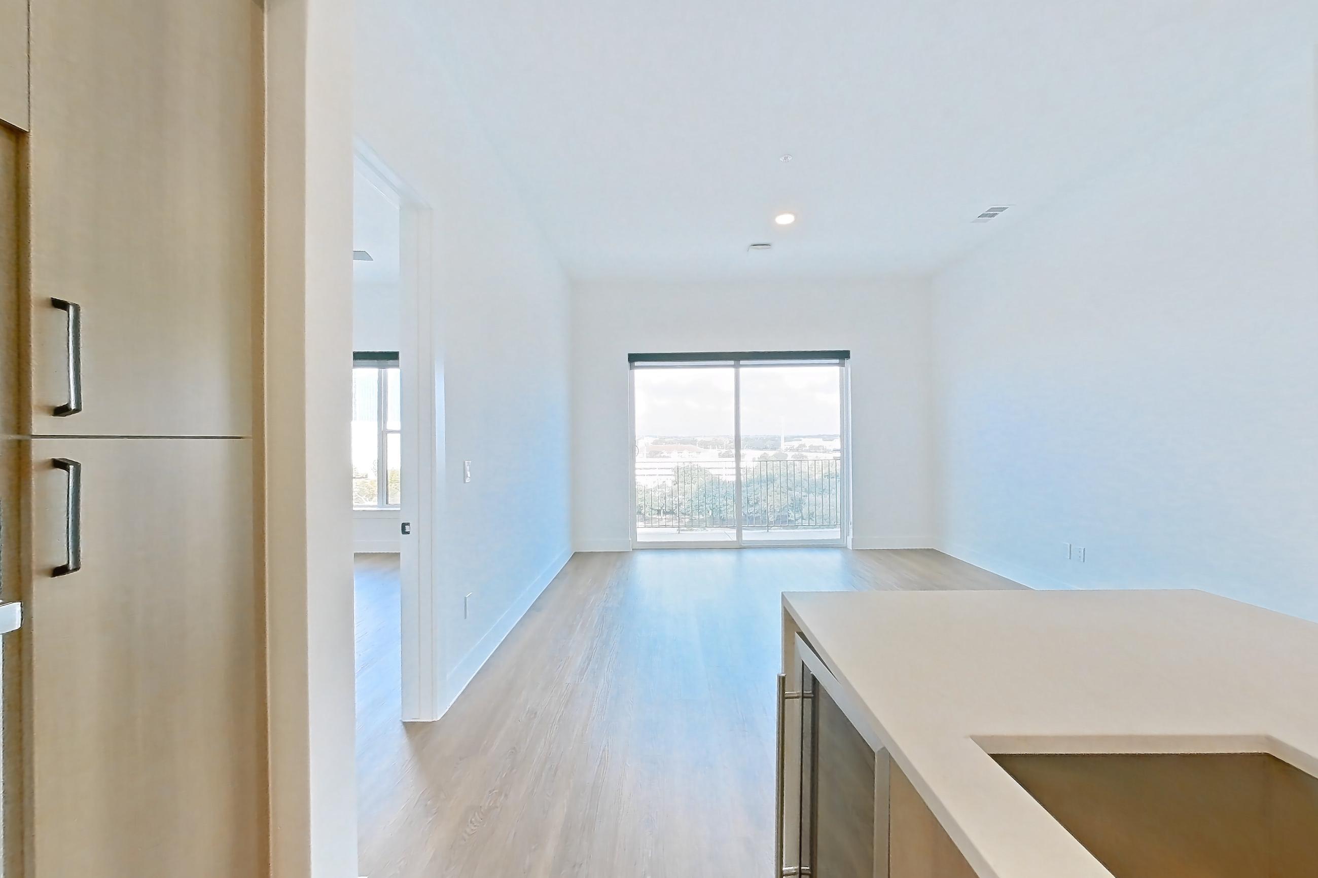 Kitchen with black appliances, built-in microwave, cooktop, electric cooktop, kitchen island, light countertops, light stone countertops, light wood-finish flooring, microwave, oven/range, and stainless steel appliances, Apartment 709 at The Watson