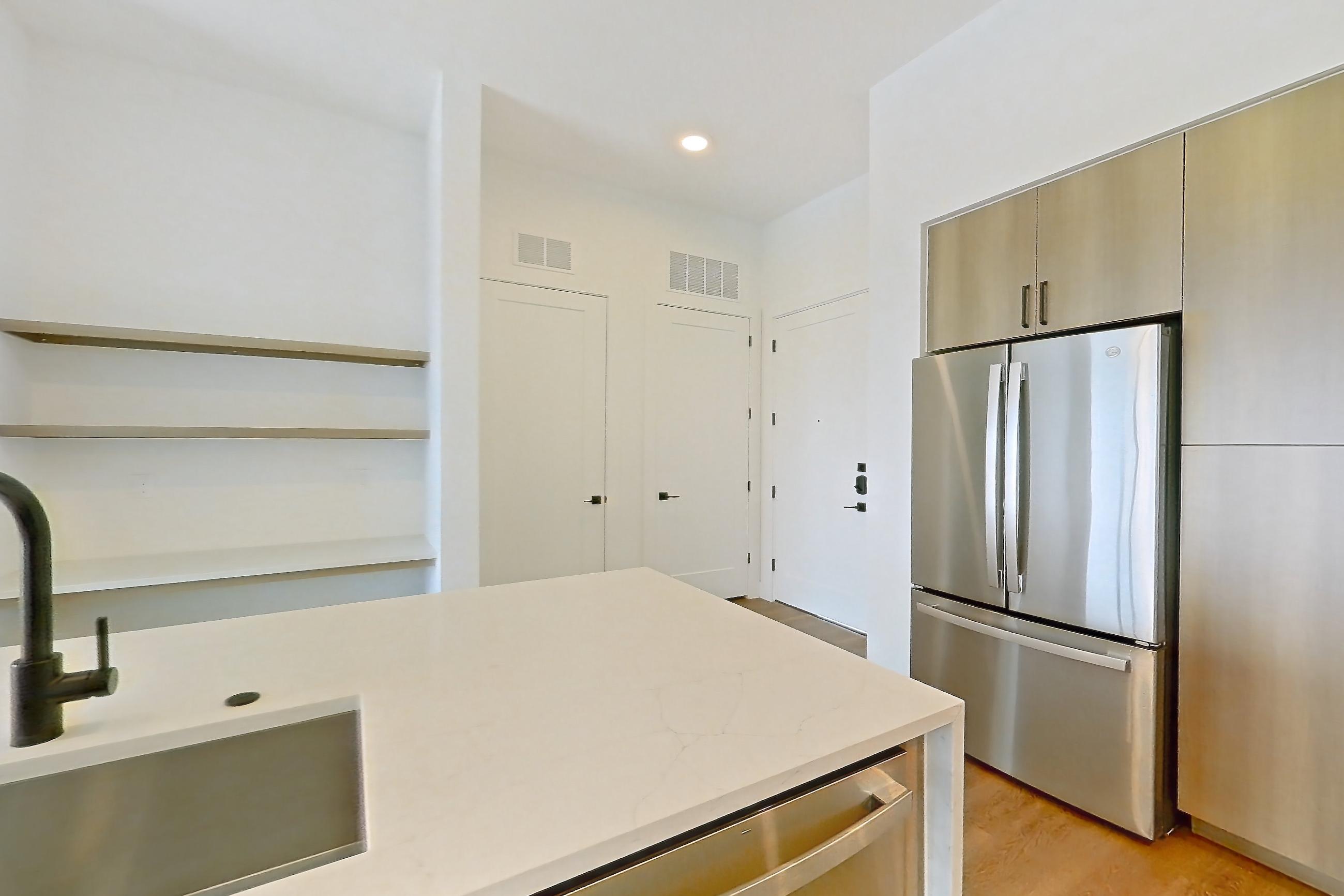 Kitchen with black appliances, built-in microwave, cooktop, dishwasher, electric cooktop, kitchen island, light countertops, light stone countertops, light wood-finish flooring, microwave, oven/range, and stainless steel appliances, Apartment 711 at The Watson