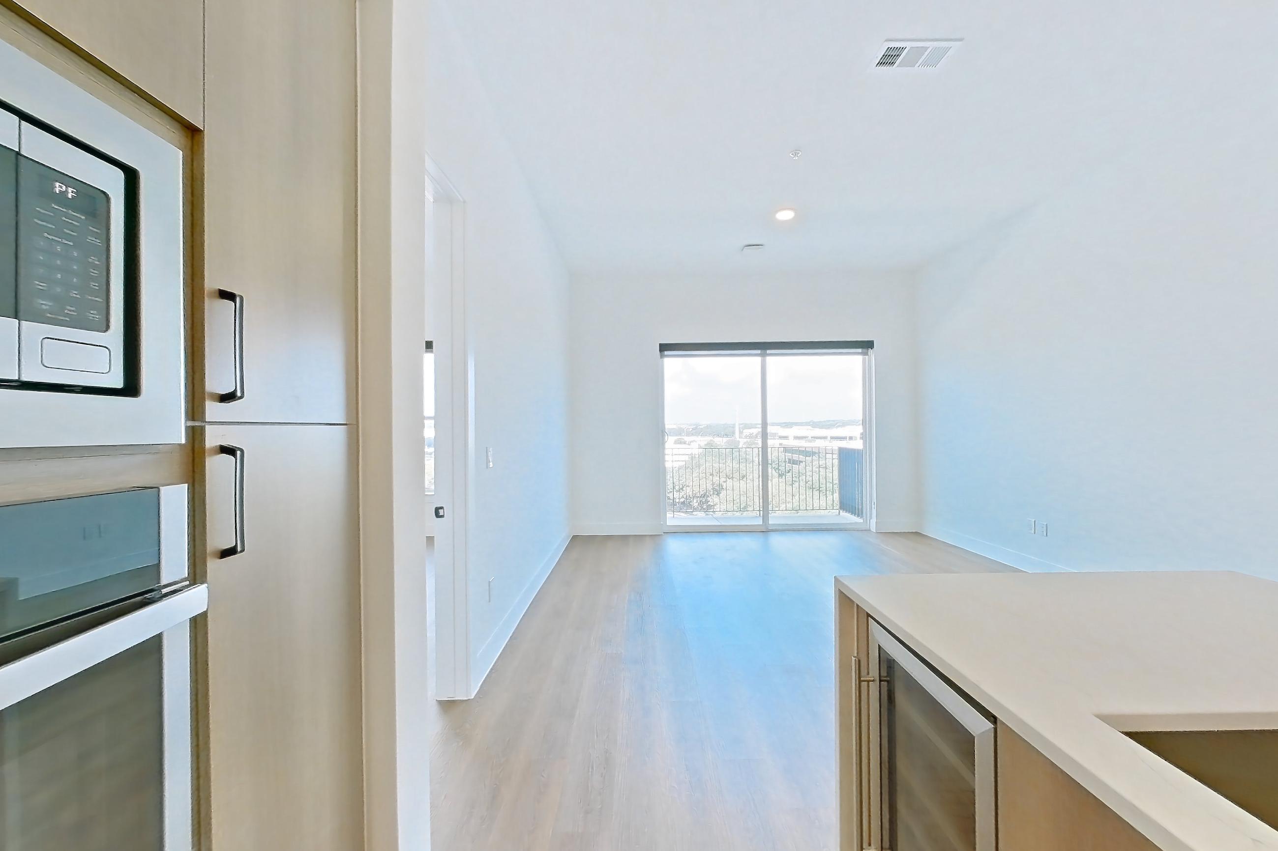 Kitchen with black appliances, built-in microwave, cooktop, dishwasher, electric cooktop, kitchen island, light countertops, light stone countertops, light wood-finish flooring, microwave, oven/range, and stainless steel appliances, Apartment 711 at The Watson