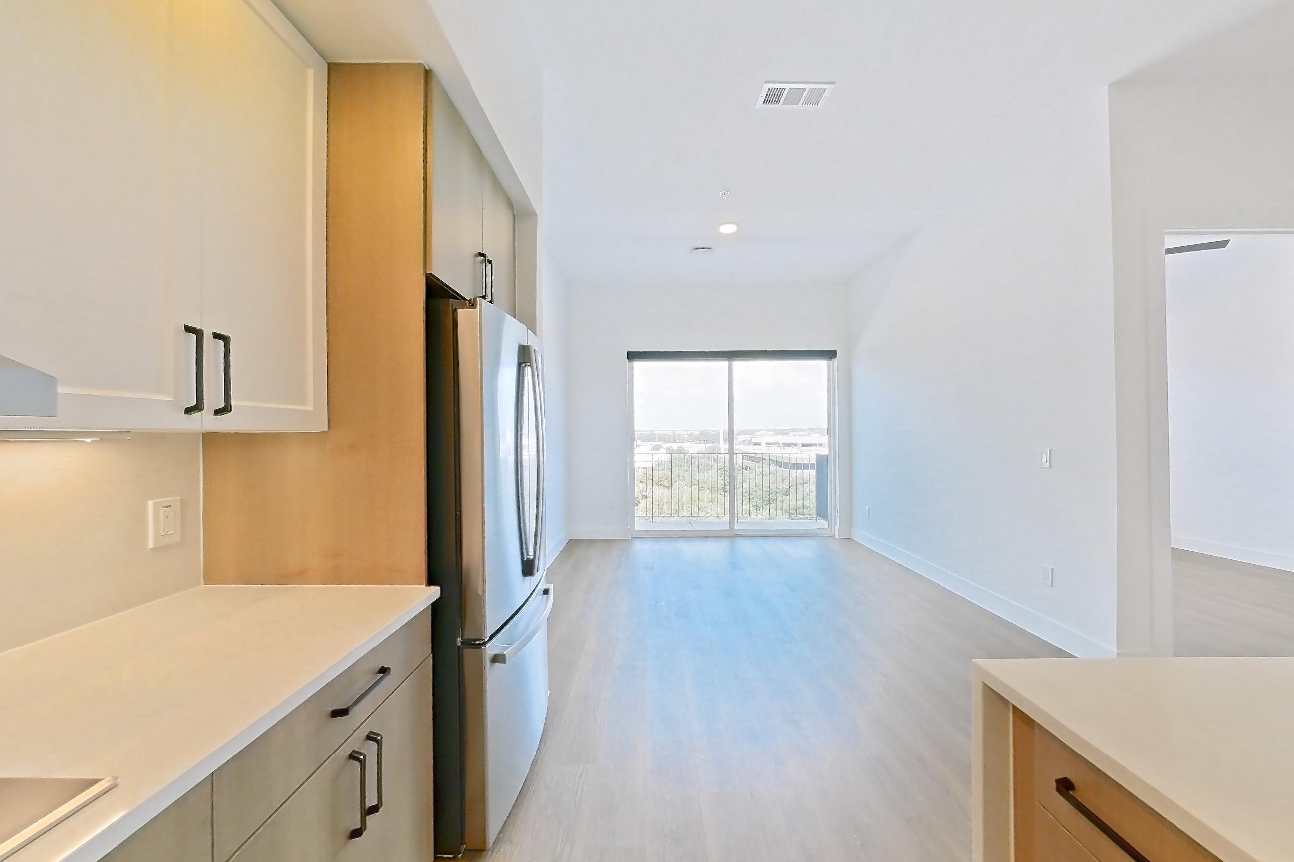 Kitchen with black appliances, cooktop, dishwasher, electric cooktop, kitchen island, light countertops, light stone countertops, light wood-finish flooring, range hood, refrigerator, and stainless steel appliances, Apartment 715 at The Watson