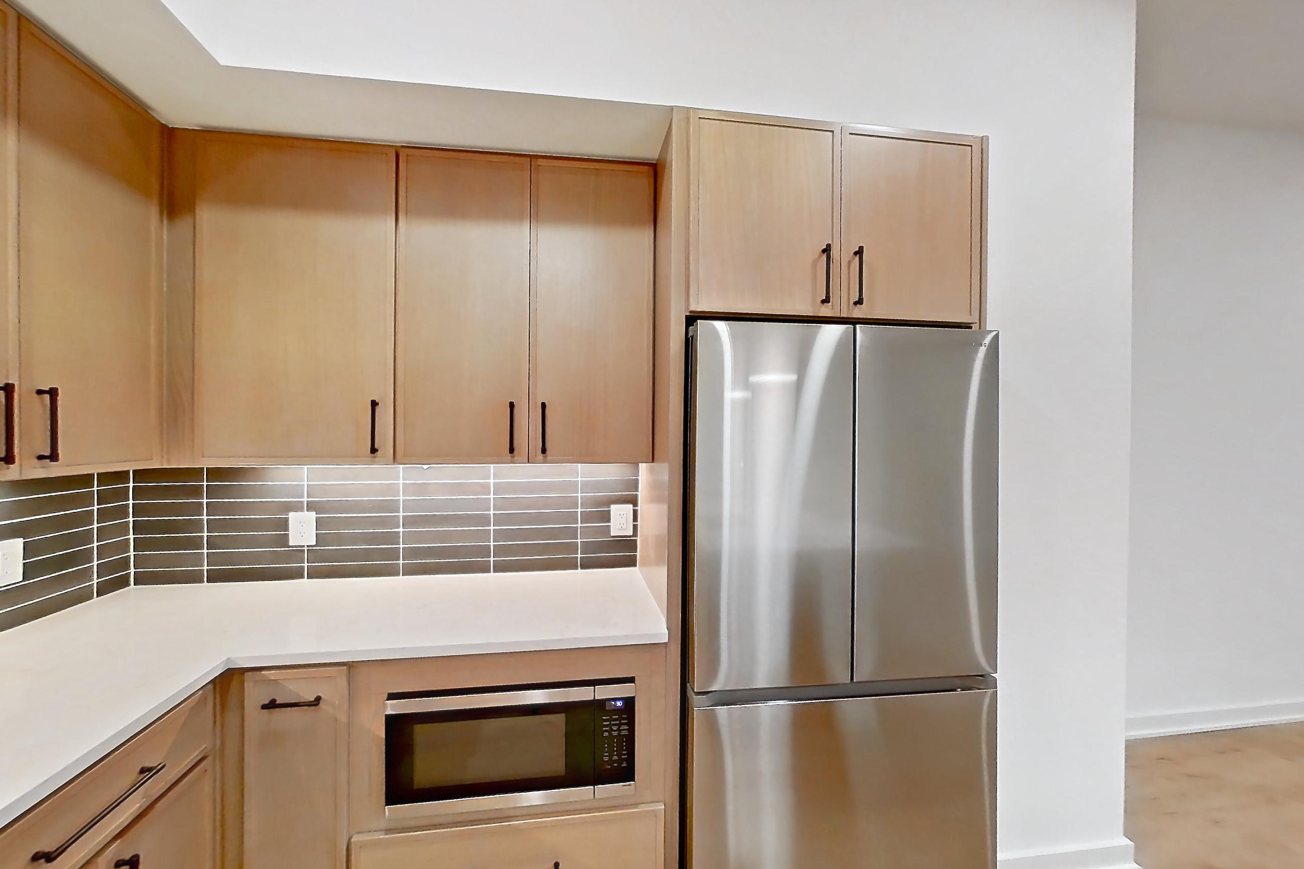Kitchen with built-in microwave, kitchen island, light countertops, light stone countertops, light wood-finish flooring, microwave, oven/range, refrigerator, and stainless steel appliances, Apartment 1103 at Cortland Galleria