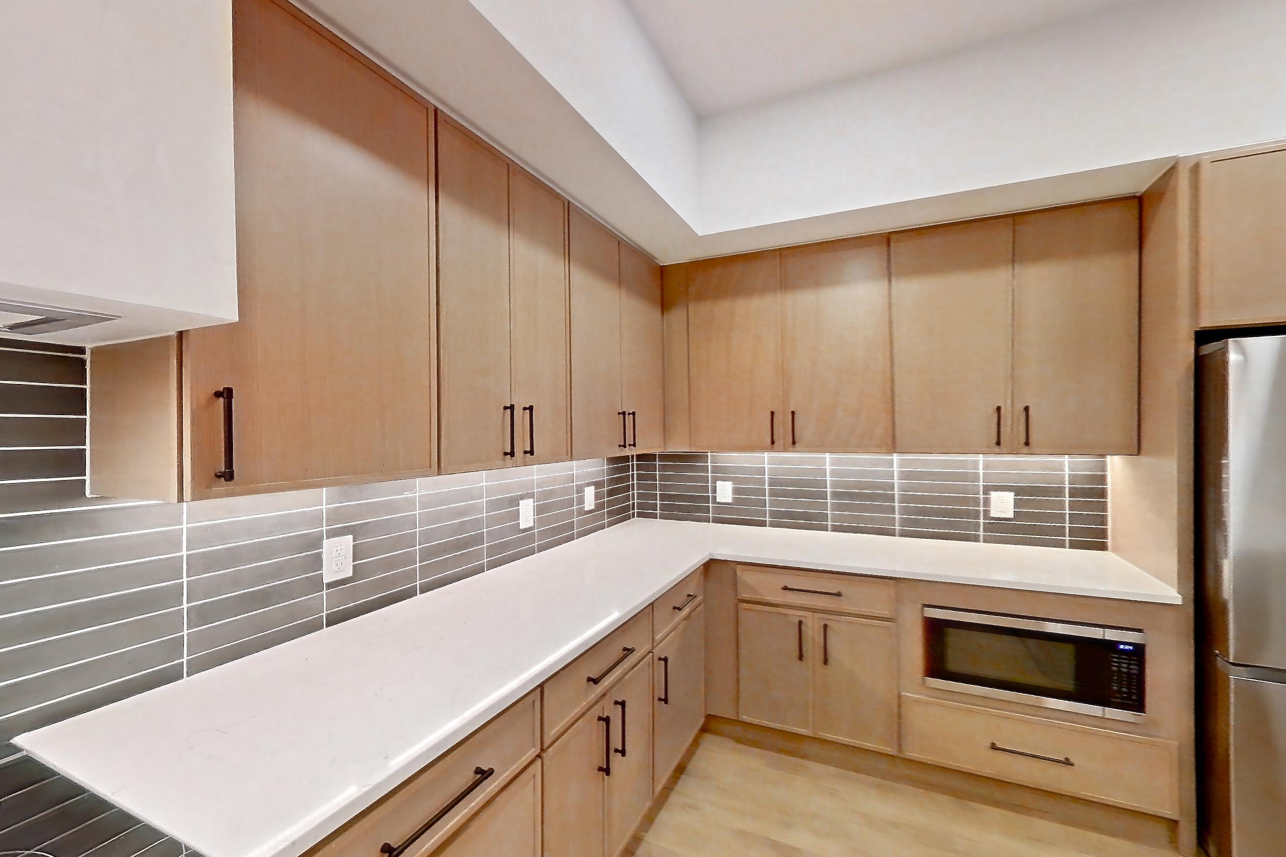Kitchen with built-in microwave, dishwasher, kitchen island, light countertops, light stone countertops, light wood-finish flooring, microwave, oven/range, refrigerator, and stainless steel appliances, Apartment 1105 at Cortland Galleria