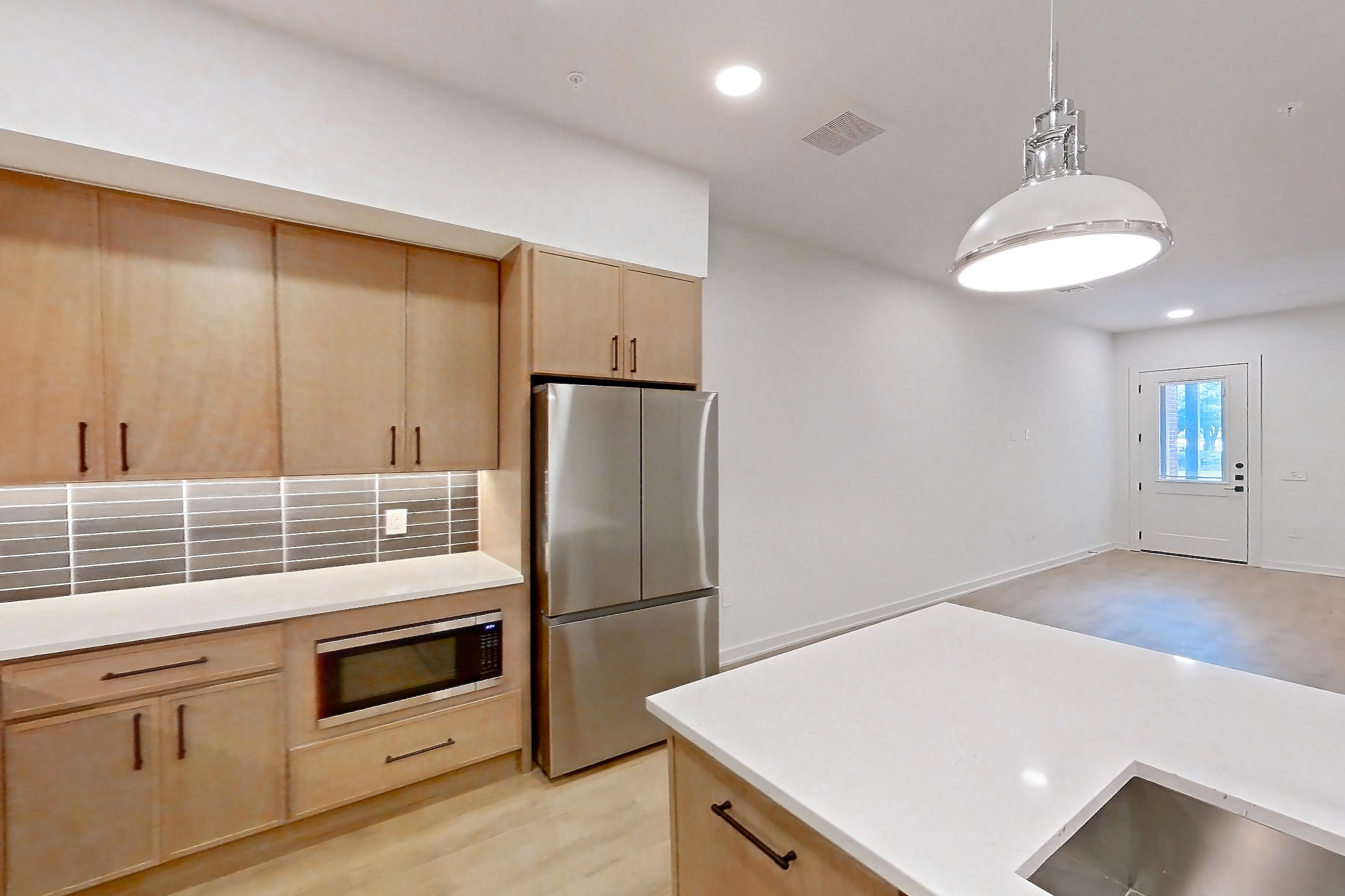Kitchen with built-in microwave, dishwasher, kitchen island, light countertops, light stone countertops, light wood-finish flooring, microwave, oven/range, refrigerator, and stainless steel appliances, Apartment 1105 at Cortland Galleria