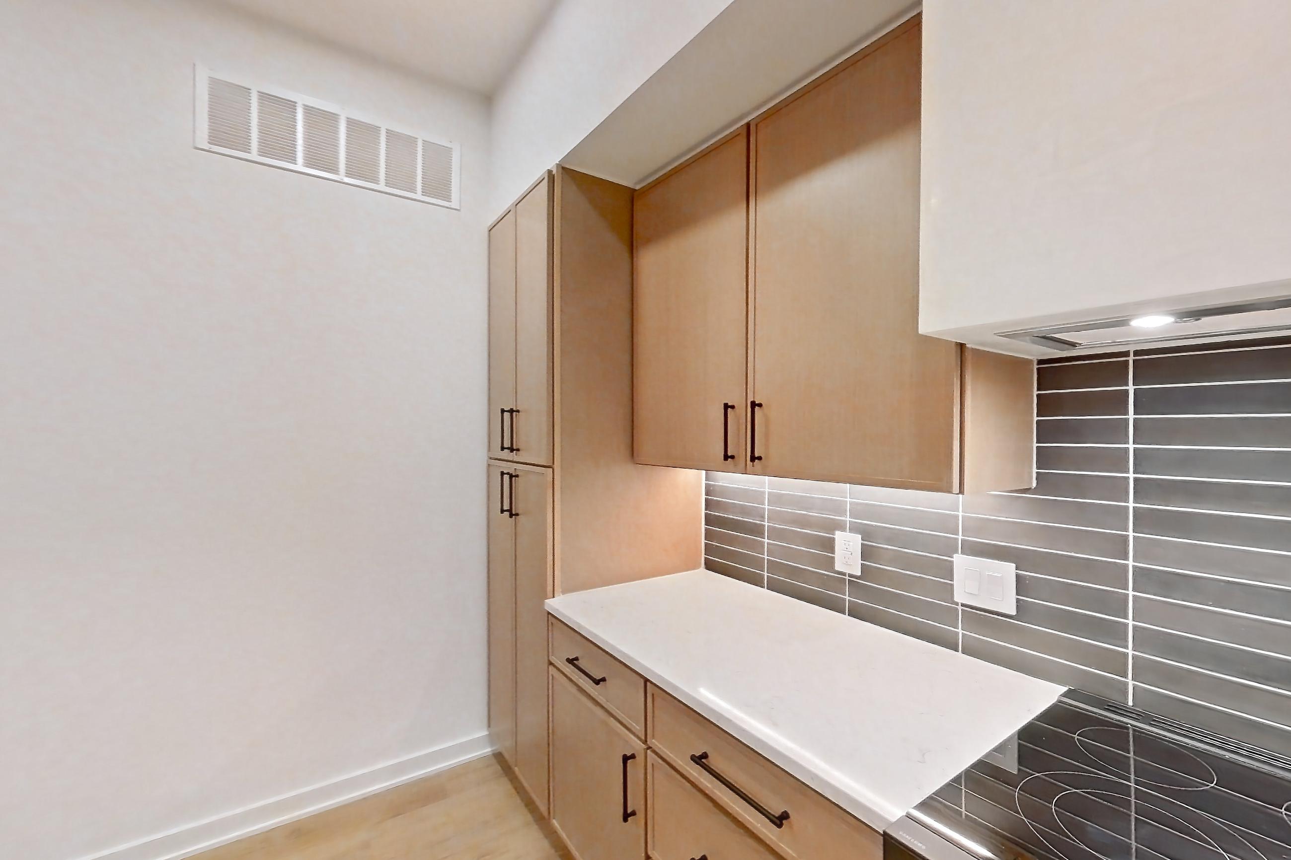 Kitchen with built-in microwave, dishwasher, kitchen island, light countertops, light stone countertops, light wood-finish flooring, microwave, oven/range, refrigerator, and stainless steel appliances, Apartment 1105 at Cortland Galleria