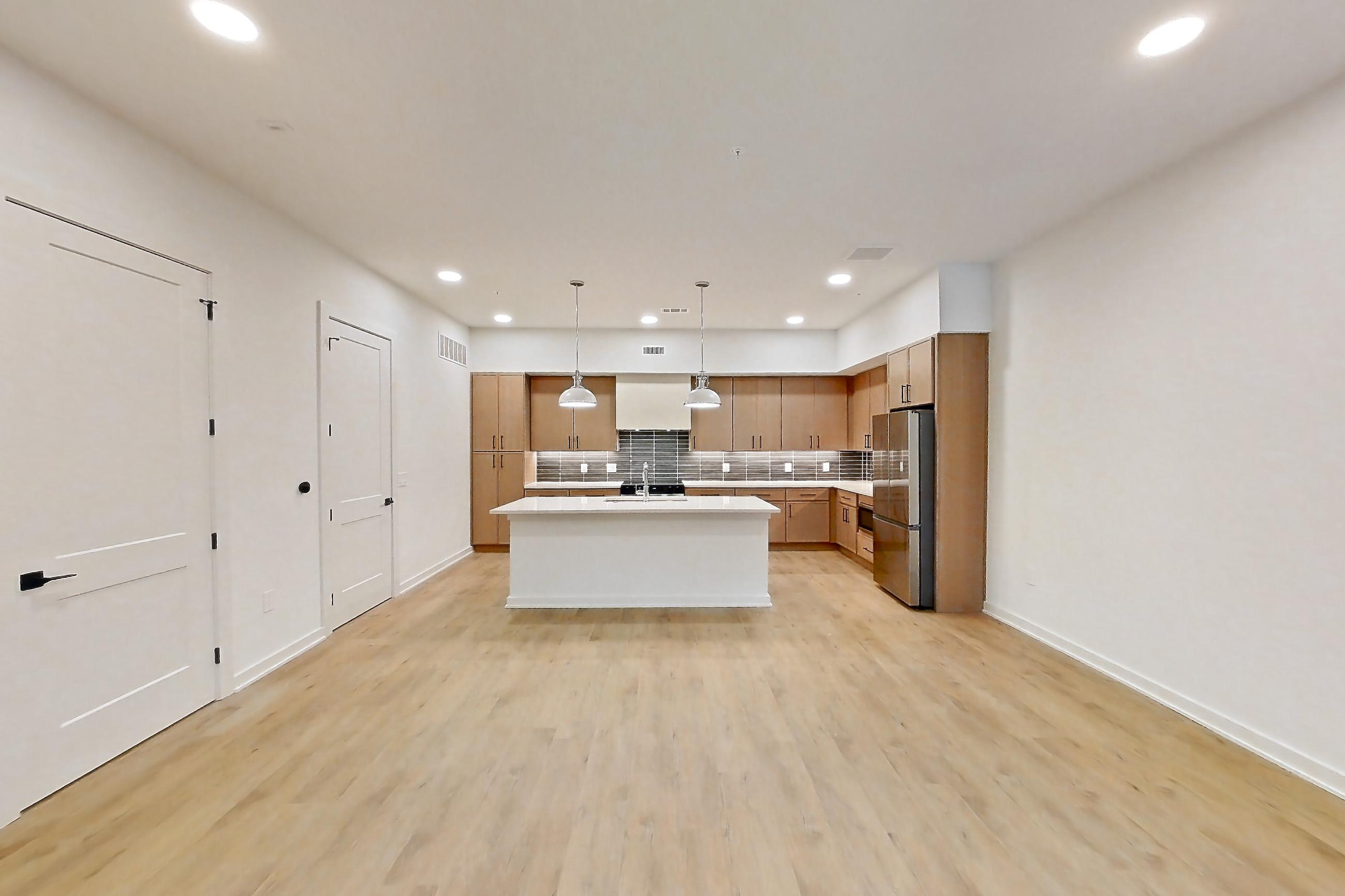 Living room with kitchen island, light countertops, light wood-finish flooring, refrigerator, and stainless steel appliances, Apartment 1105 at Cortland Galleria