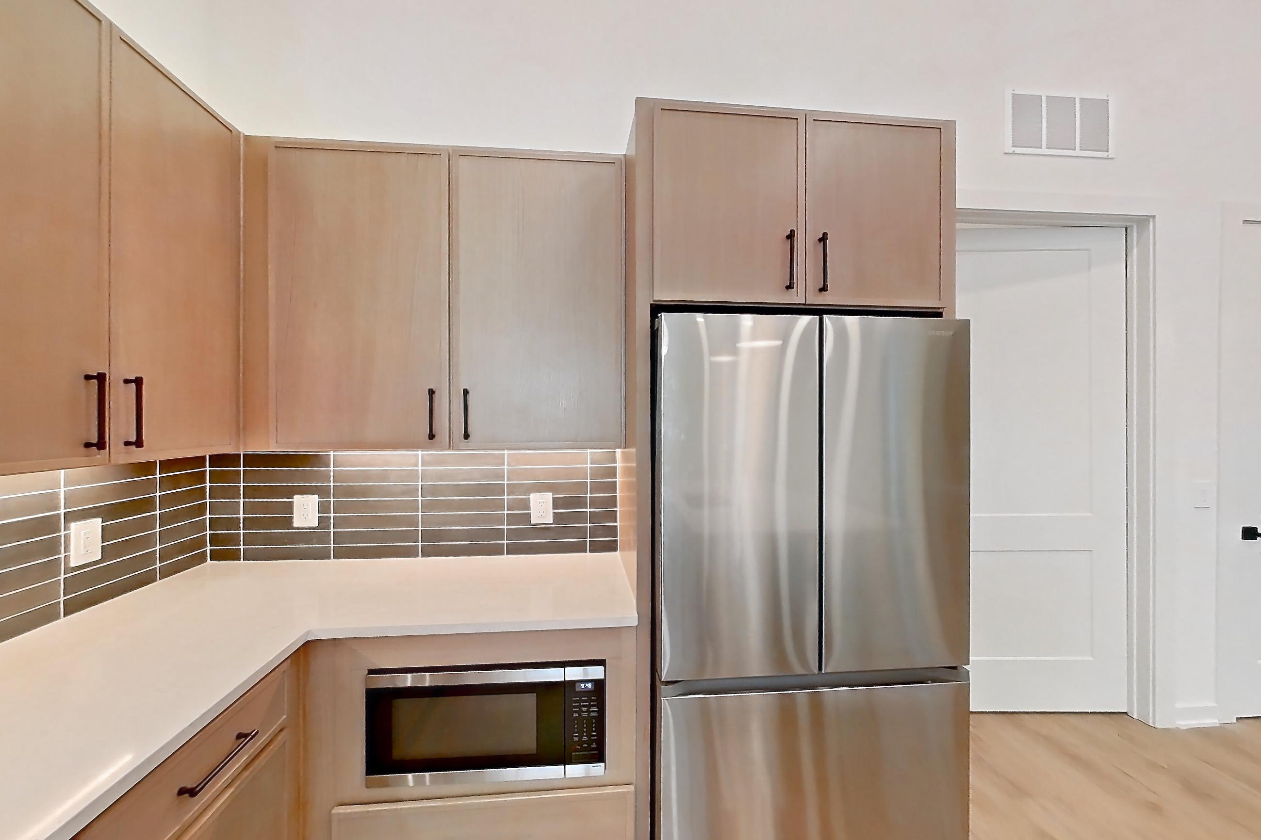 Kitchen with built-in microwave, electric range, kitchen island, light countertops, light stone countertops, light wood-finish flooring, microwave, oven/range, refrigerator, and stainless steel appliances, Apartment 1117 at Cortland Galleria