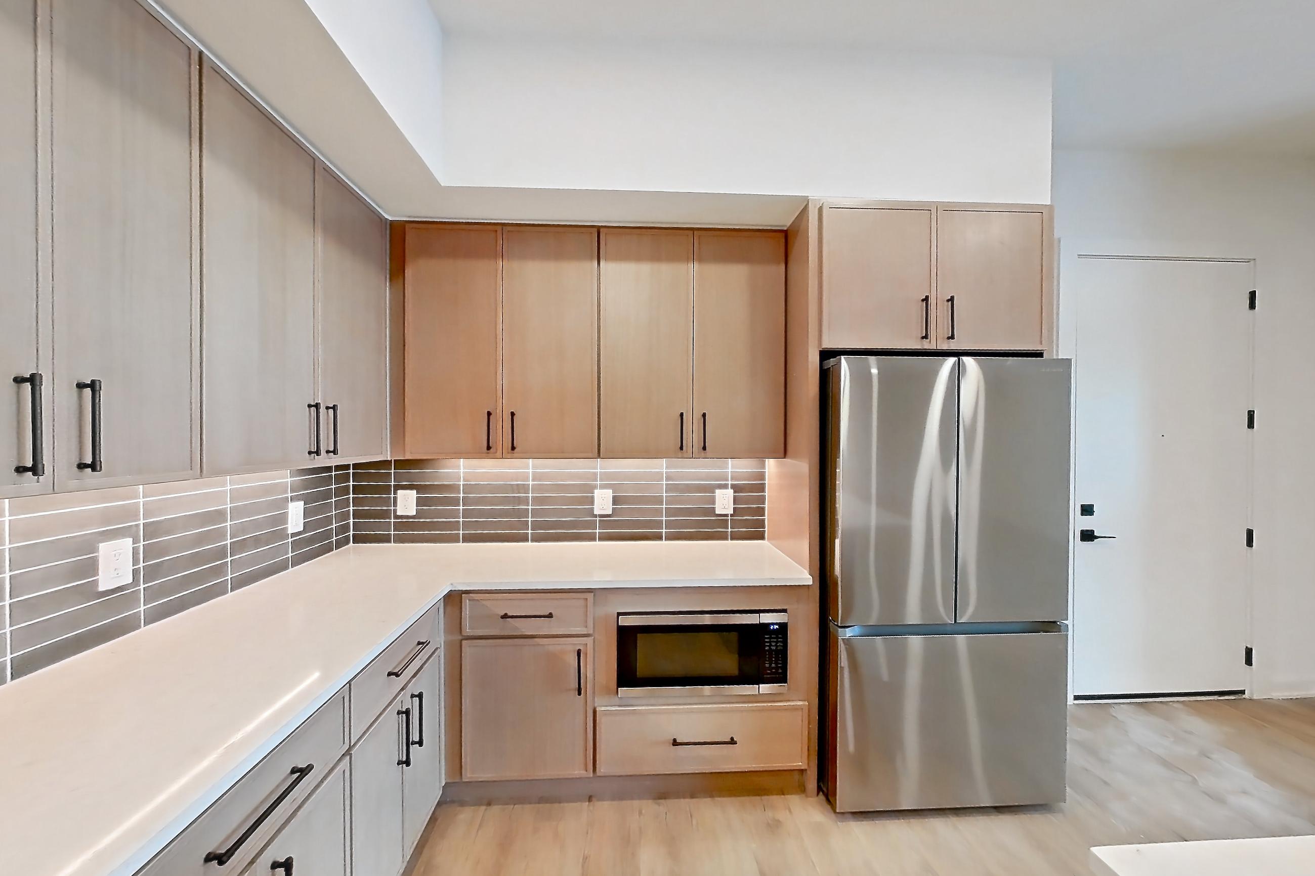 Kitchen with electric range, kitchen island, light countertops, light stone countertops, light wood-finish flooring, microwave, oven/range, refrigerator, and stainless steel appliances, Apartment 1101 at Cortland Galleria