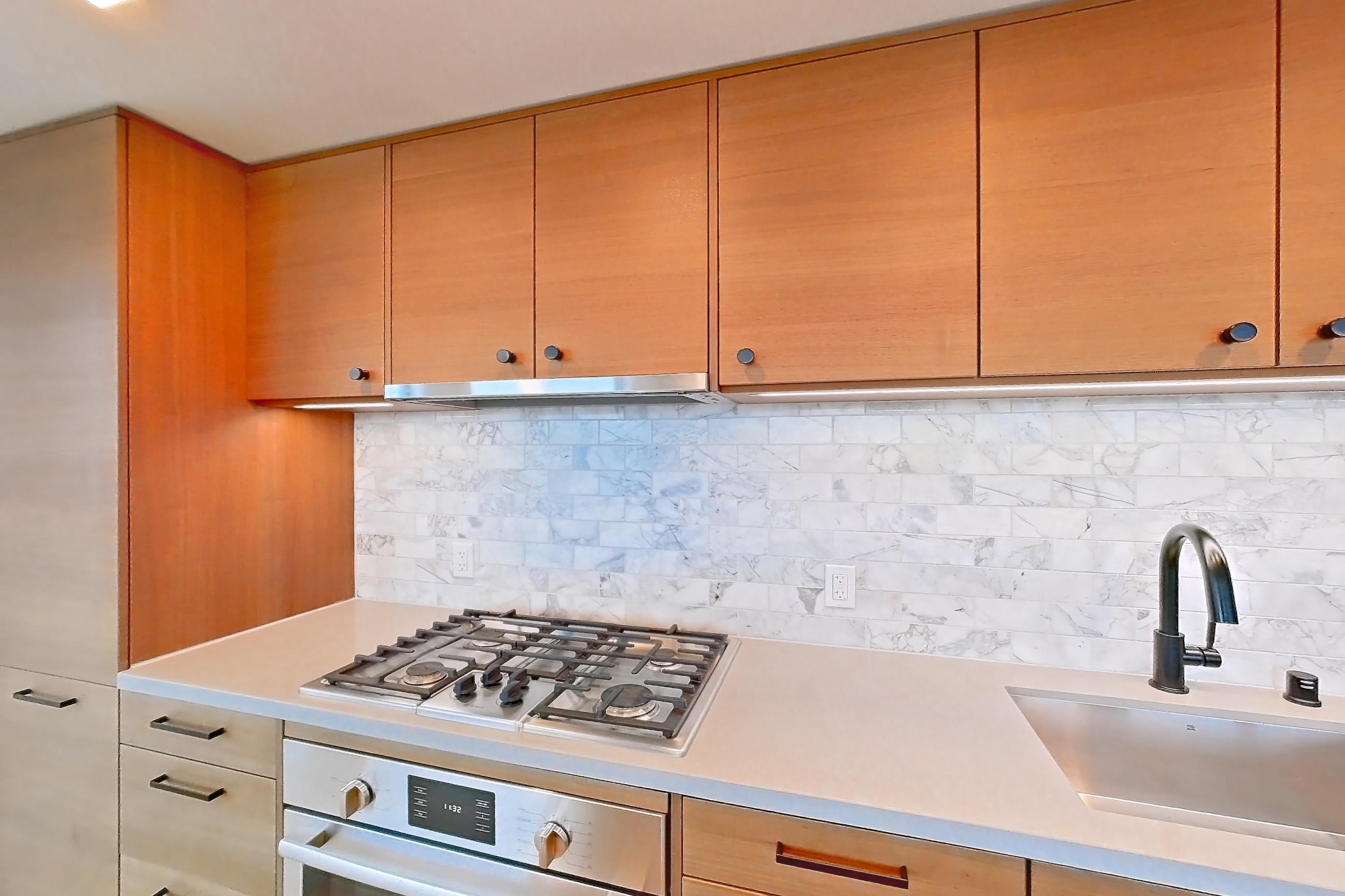 Kitchen with cooktop, gas cooktop, light countertops, light stone countertops, light wood-finish flooring, oven/range, range hood, and stainless steel appliances, Apartment PH2 at Konrad on the Park