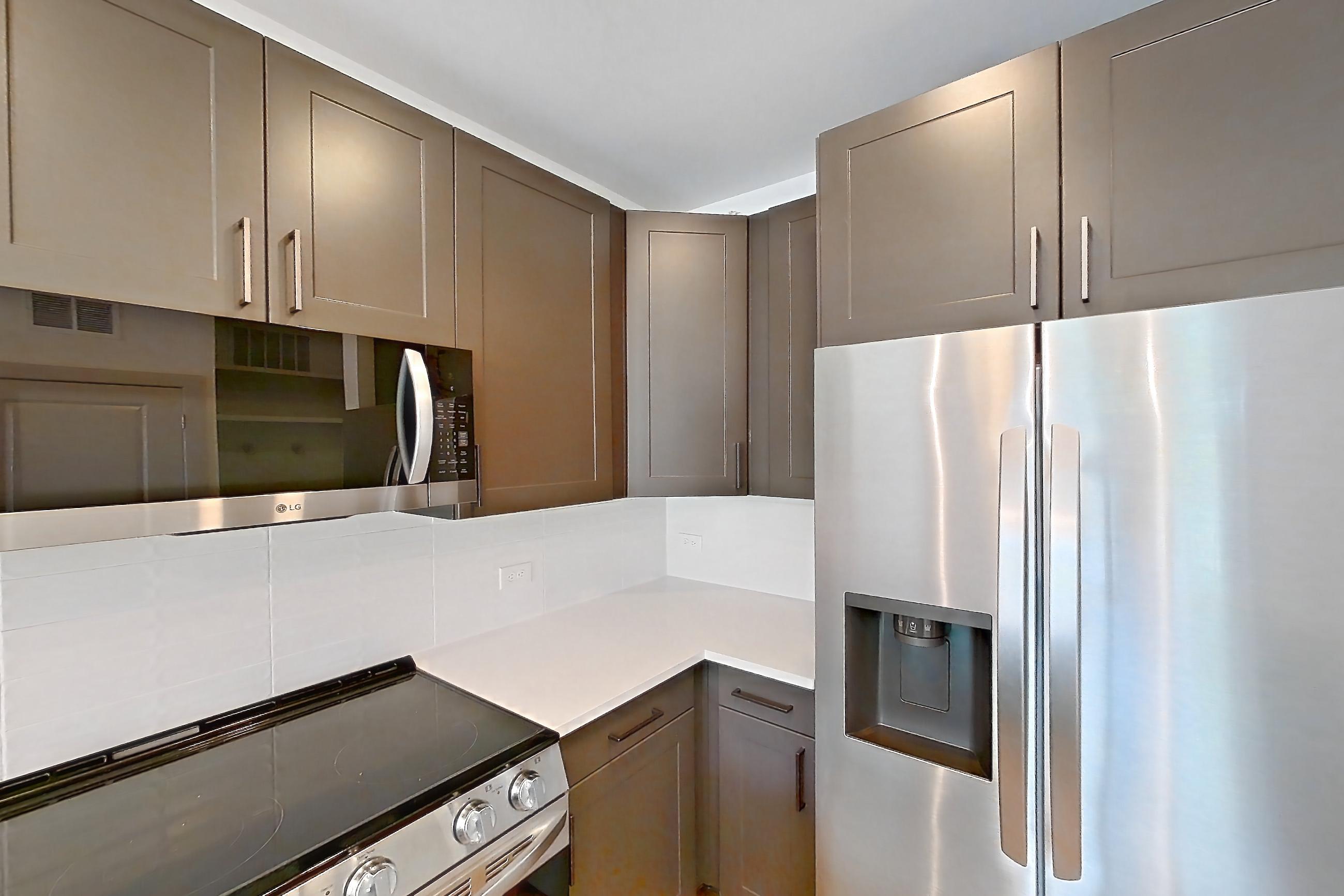 Kitchen with electric range, light countertops, light stone countertops, light wood-finish flooring, microwave, oven/range, refrigerator, stainless steel appliances, and water & ice dispenser, Apartment 2246 at Groves South Congress