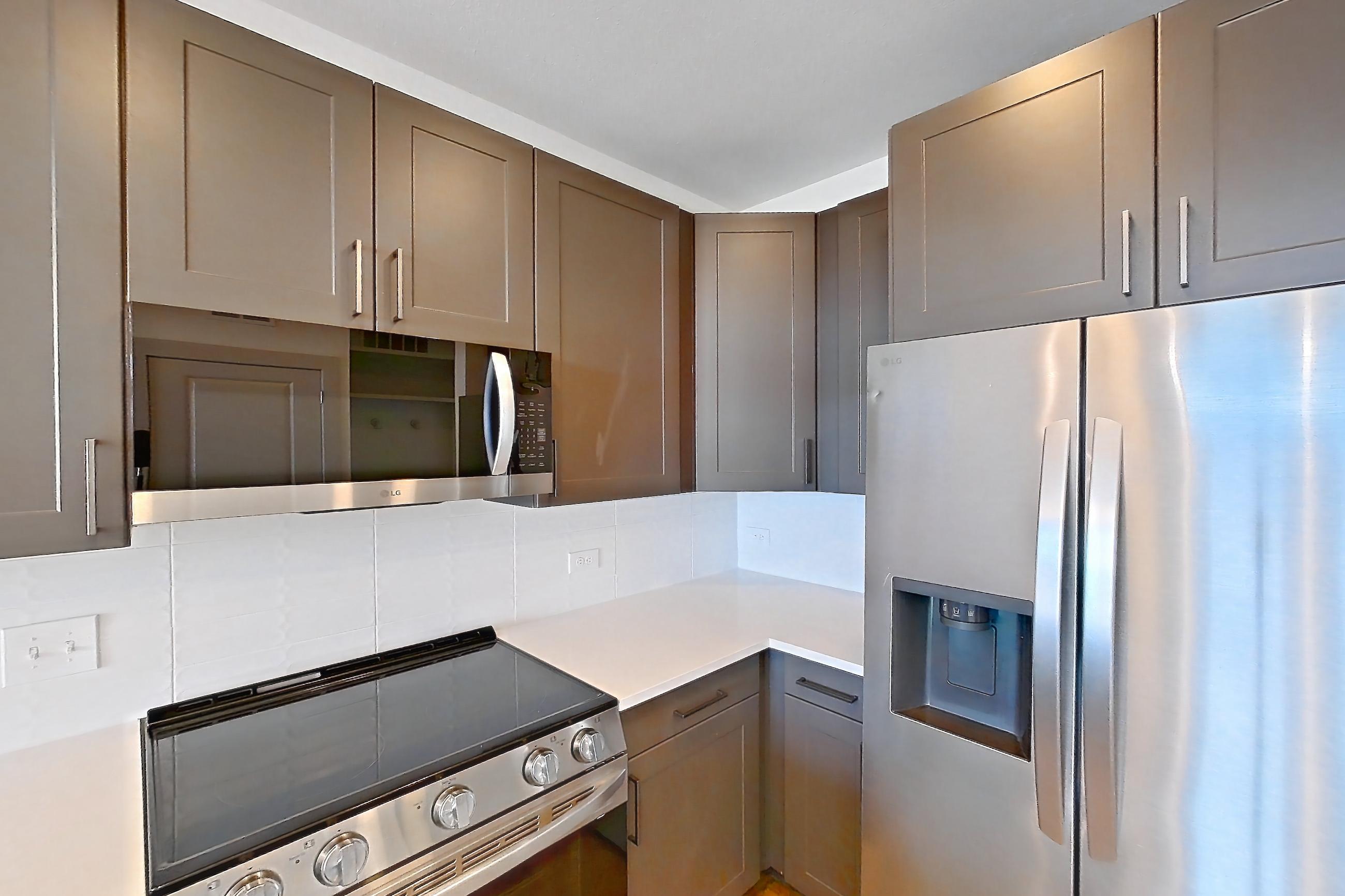 Kitchen with dishwasher, electric range, light countertops, light wood-finish flooring, microwave, oven/range, refrigerator, stainless steel appliances, and water & ice dispenser, Apartment 2446 at Groves South Congress
