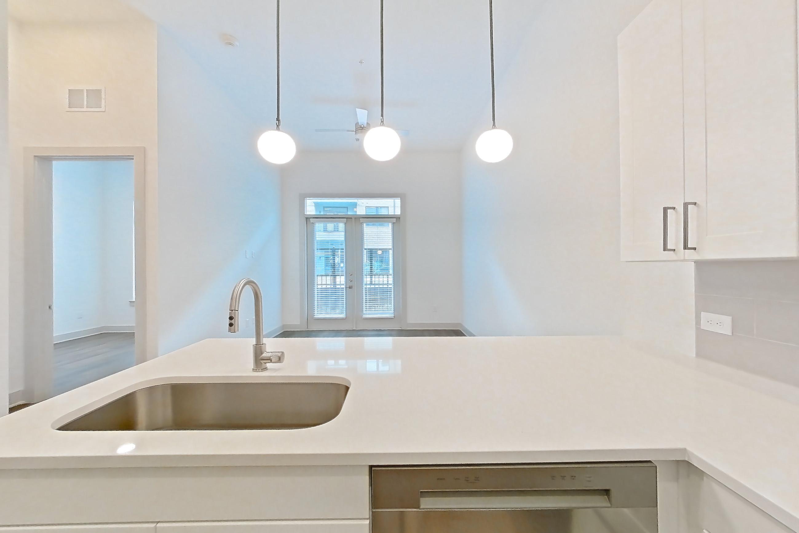 Kitchen with dishwasher, electric range, light countertops, light stone countertops, light wood-finish flooring, microwave, oven/range, and stainless steel appliances, Apartment 2144 at Groves South Congress