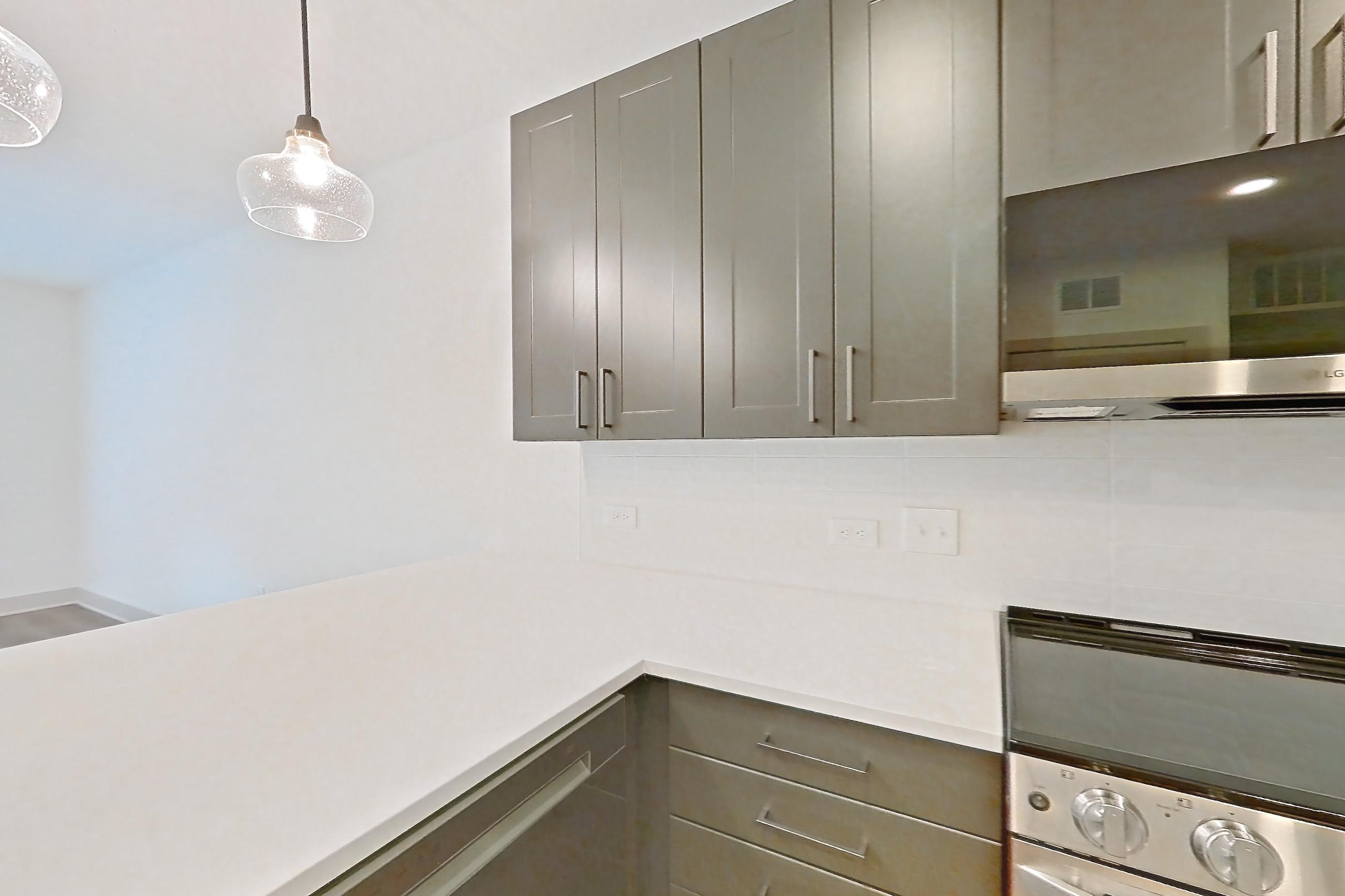 Kitchen with dishwasher, electric range, kitchen island, light countertops, light stone countertops, light wood-finish flooring, microwave, oven/range, and stainless steel appliances, Apartment 2244 at Groves South Congress