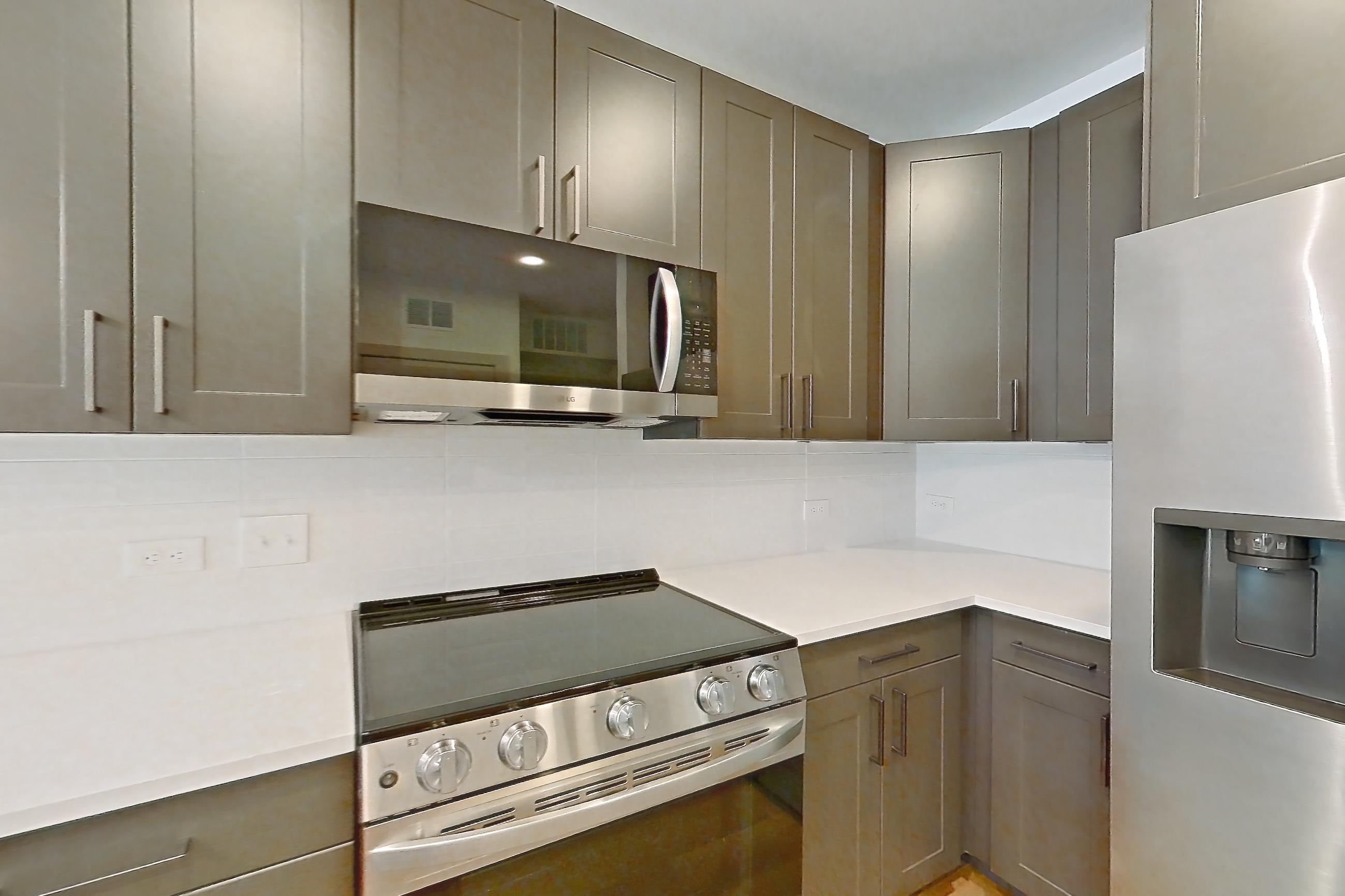 Kitchen with dishwasher, electric range, kitchen island, light countertops, light stone countertops, light wood-finish flooring, microwave, oven/range, and stainless steel appliances, Apartment 2244 at Groves South Congress