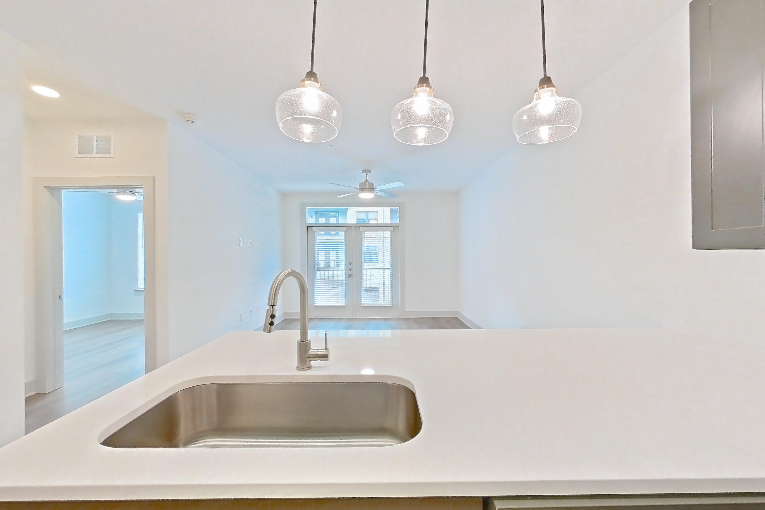 Kitchen with dishwasher, electric range, kitchen island, light countertops, light stone countertops, light wood-finish flooring, microwave, oven/range, and stainless steel appliances, Apartment 2244 at Groves South Congress