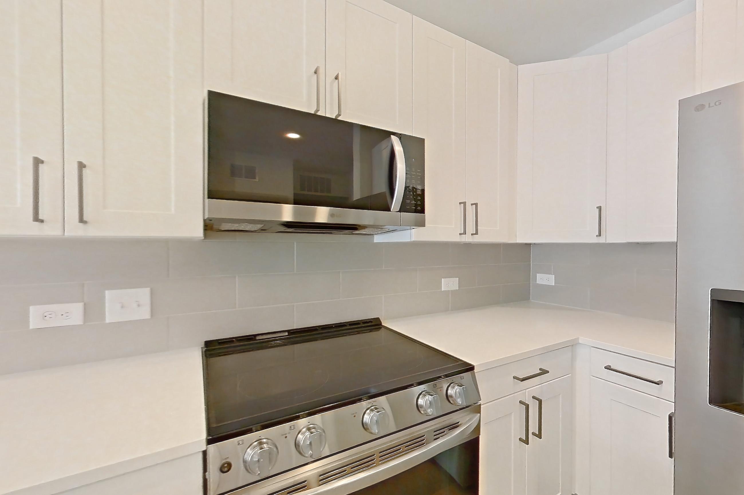 Kitchen with dishwasher, electric range, light countertops, light stone countertops, light wood-finish flooring, microwave, oven/range, and stainless steel appliances, Apartment 2344 at Groves South Congress