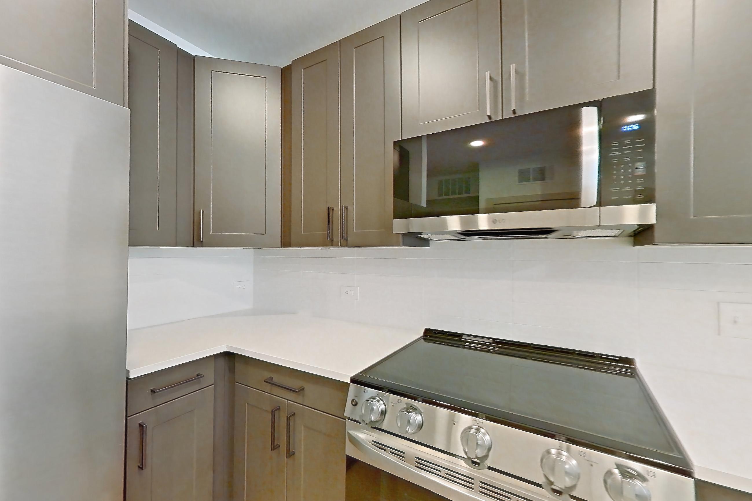 Kitchen with dishwasher, electric range, light countertops, light stone countertops, light wood-finish flooring, microwave, oven/range, and stainless steel appliances, Apartment 2205 at Groves South Congress
